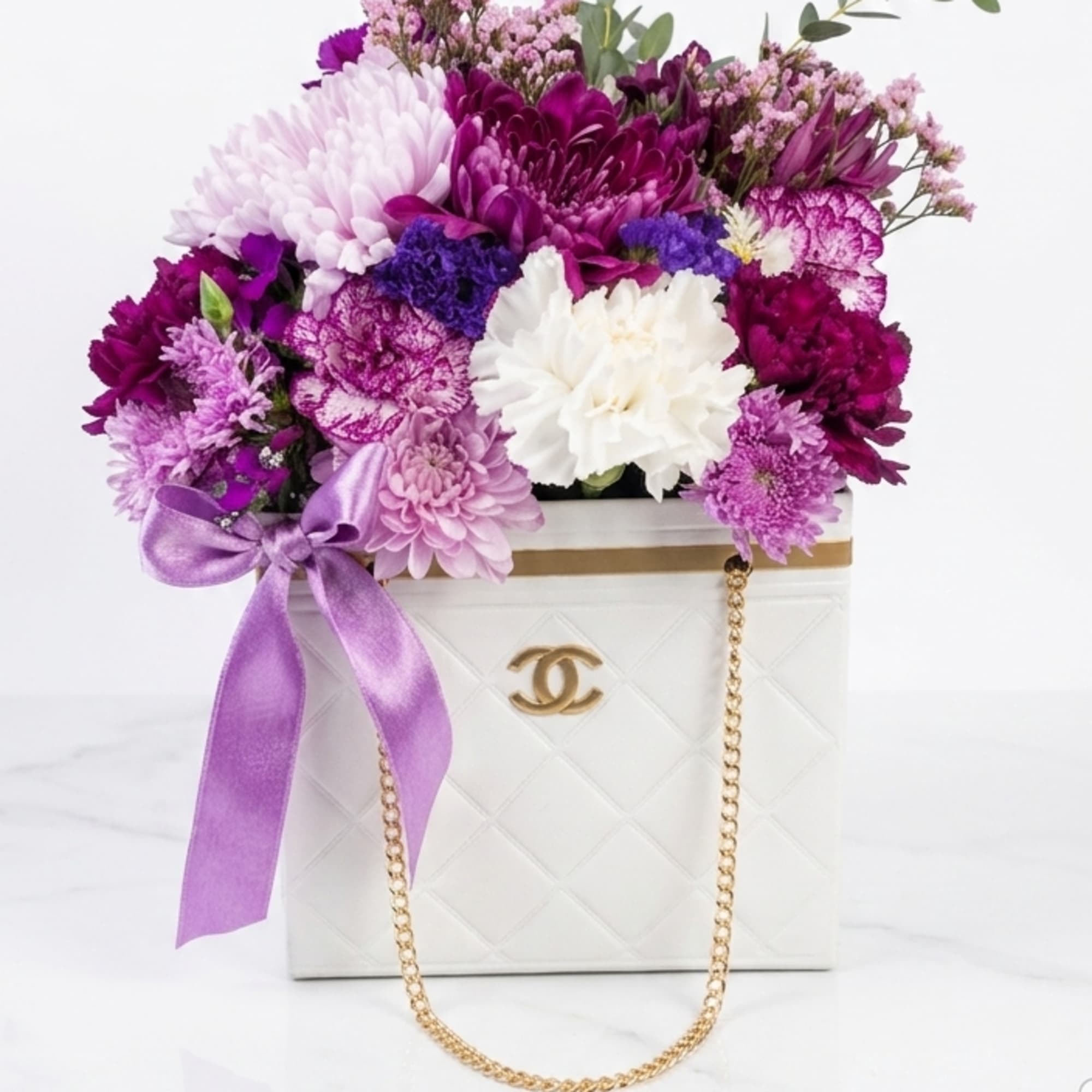 Purple and white flower arrangement in a white handbag-shaped box with a ribbon