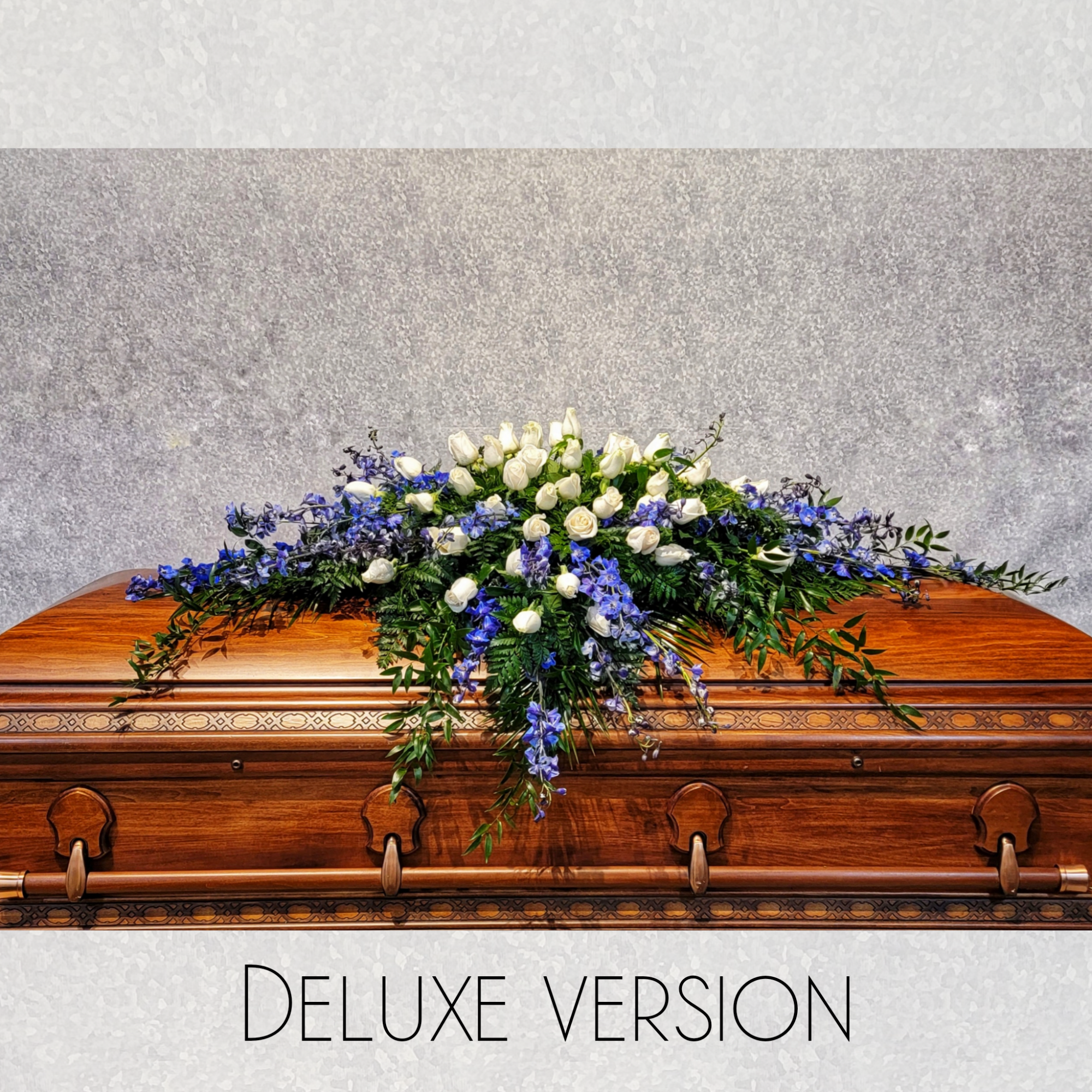 A broad, low casket spray that lays gently across a polished wooden