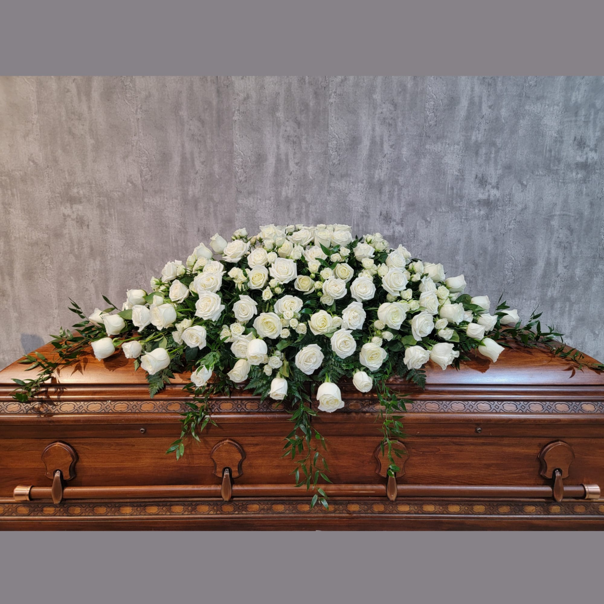 White rose casket spray with trailing greenery on a wooden casket