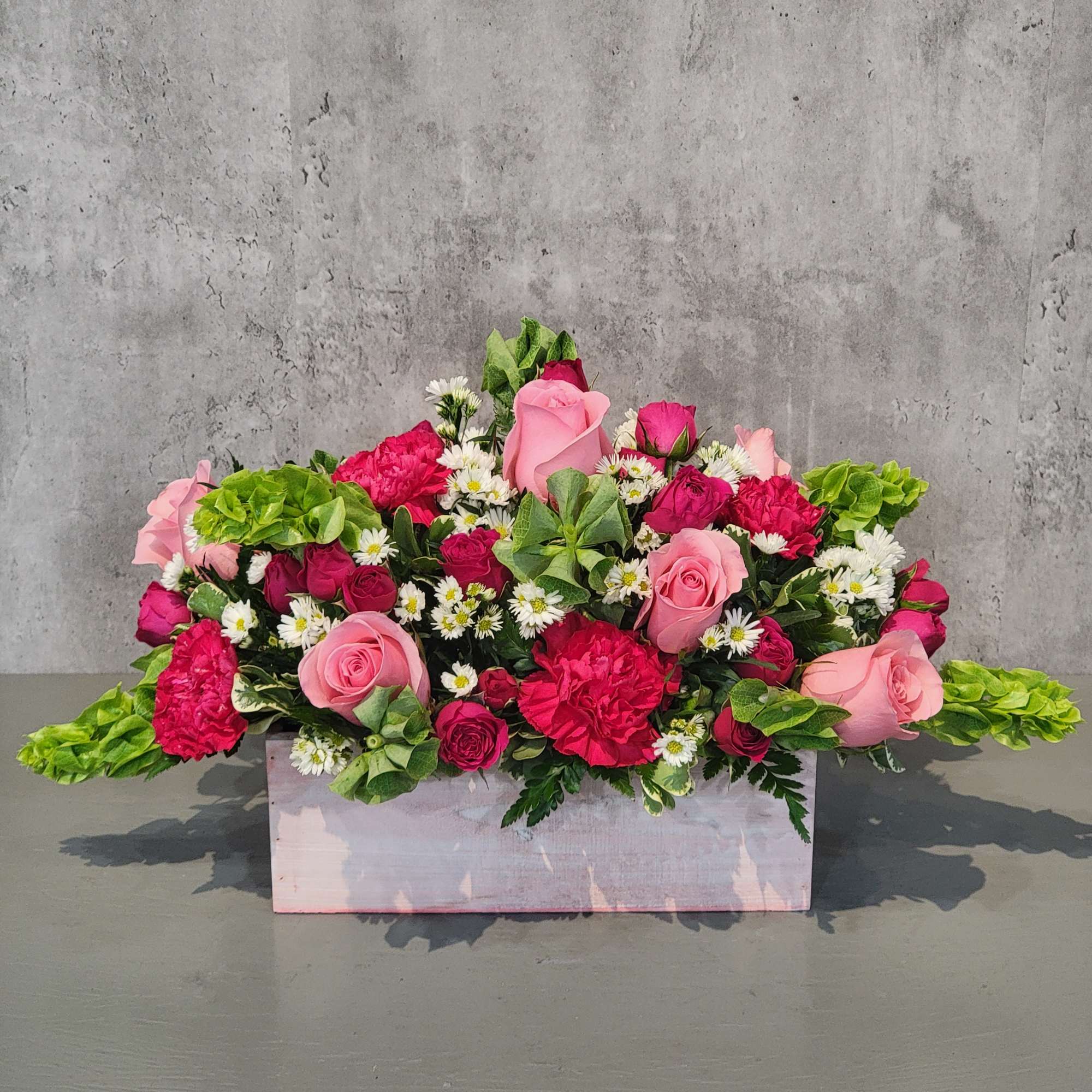 Pink and red rose arrangement in a pale wooden box with white daisies