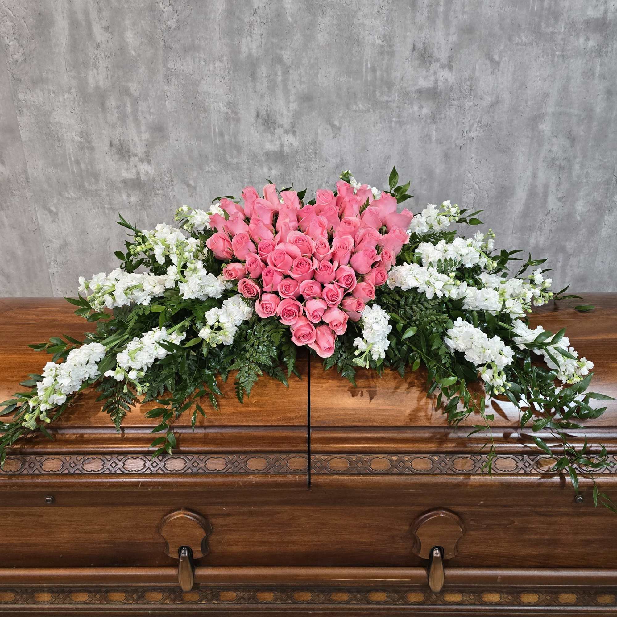 Pink rose casket spray with white flowers and greenery