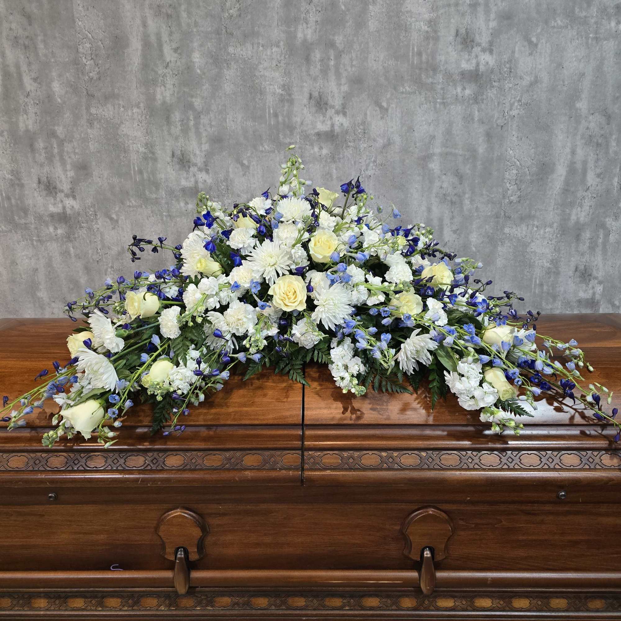White and blue floral casket spray on a wooden casket