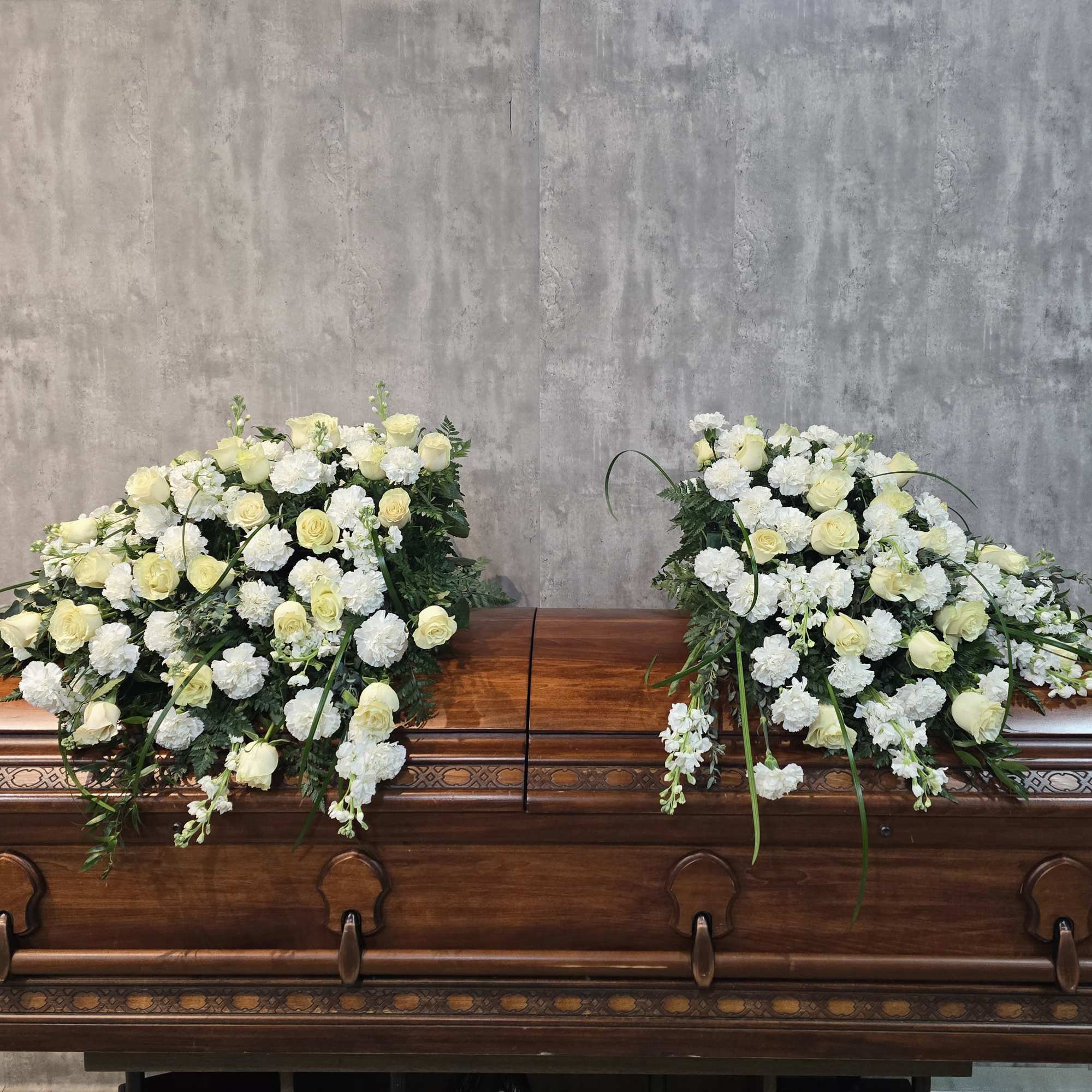 White and pale yellow floral sprays on a wooden casket