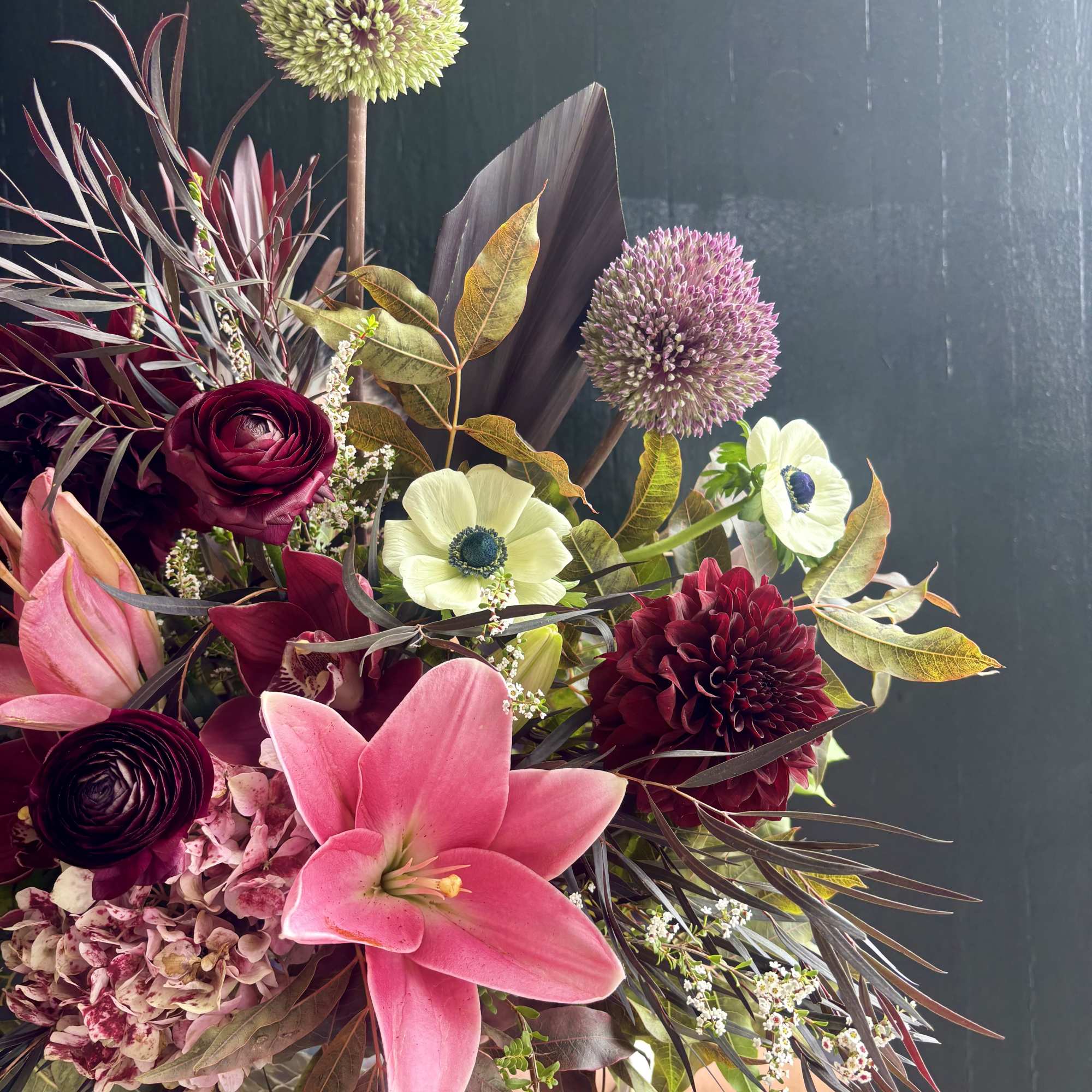 Bouquet with pink lily, dark red blooms, and round allium flowers