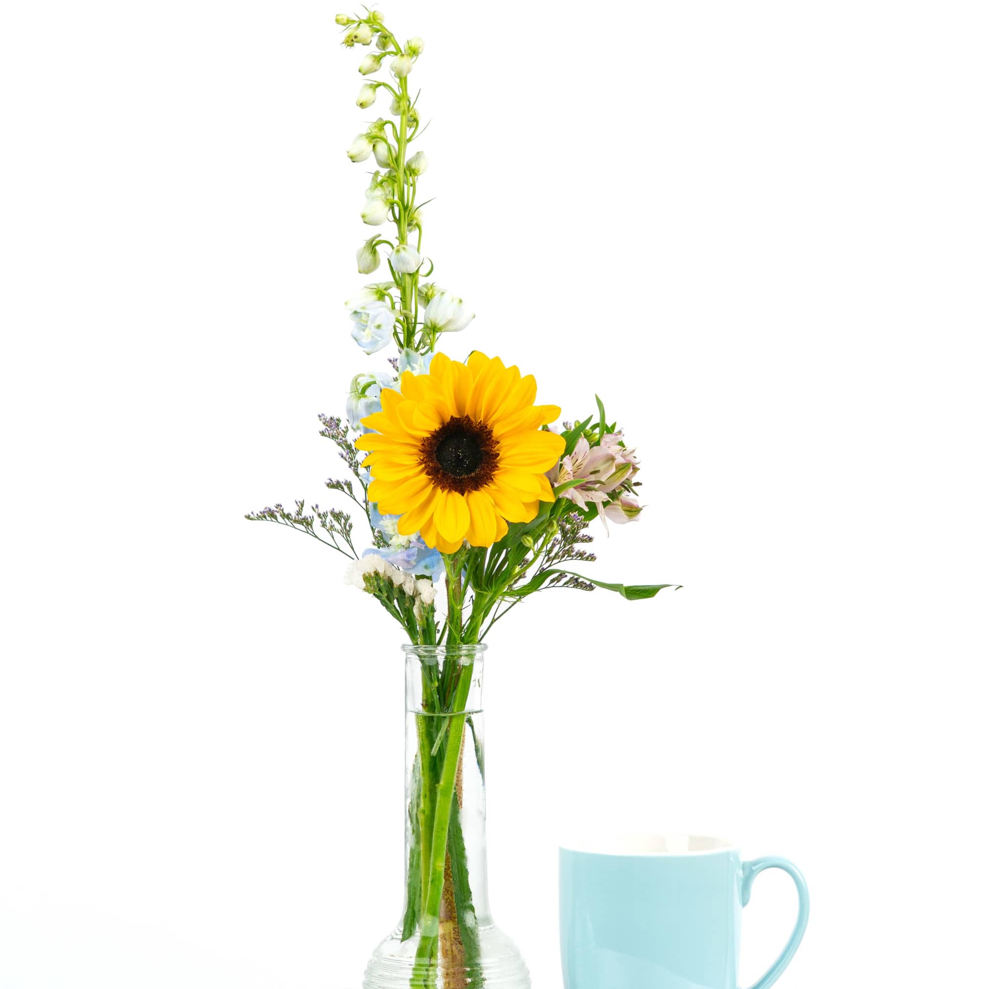 Sunflower bouquet in a clear glass vase beside a light blue mug
