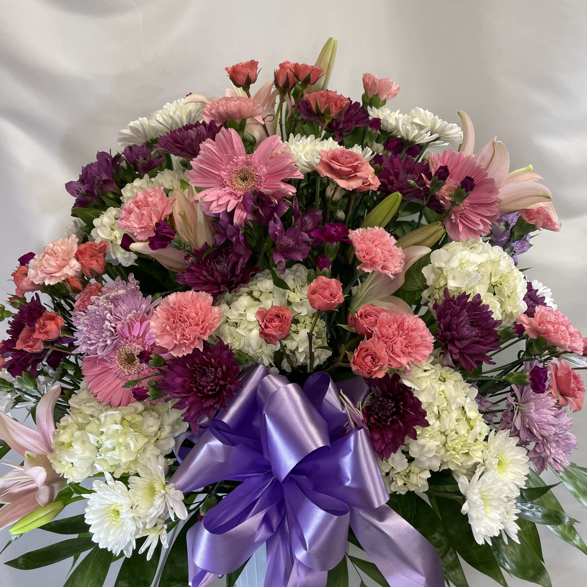Large mixed bouquet of pink, purple, and white flowers with a purple ribbon