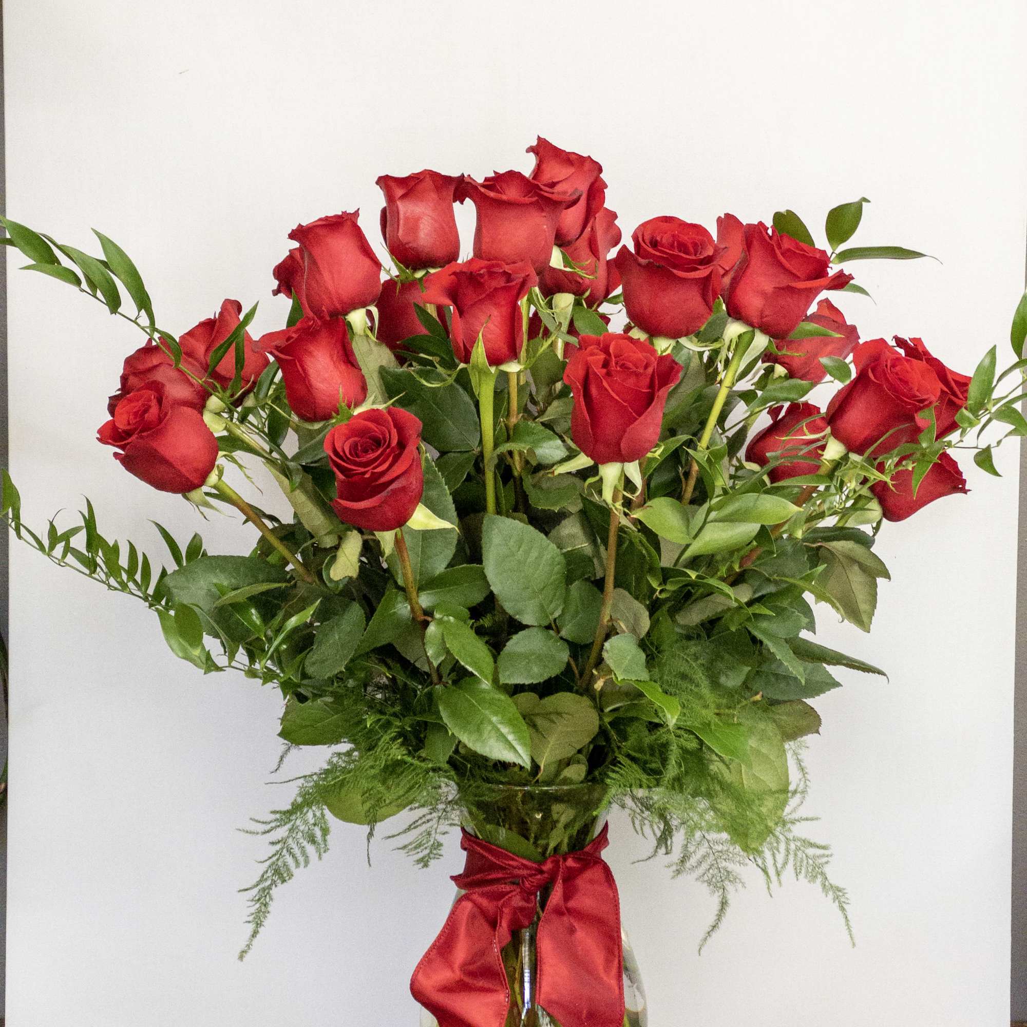 Tall arrangement of red roses in a clear glass vase with a red ribbon bow