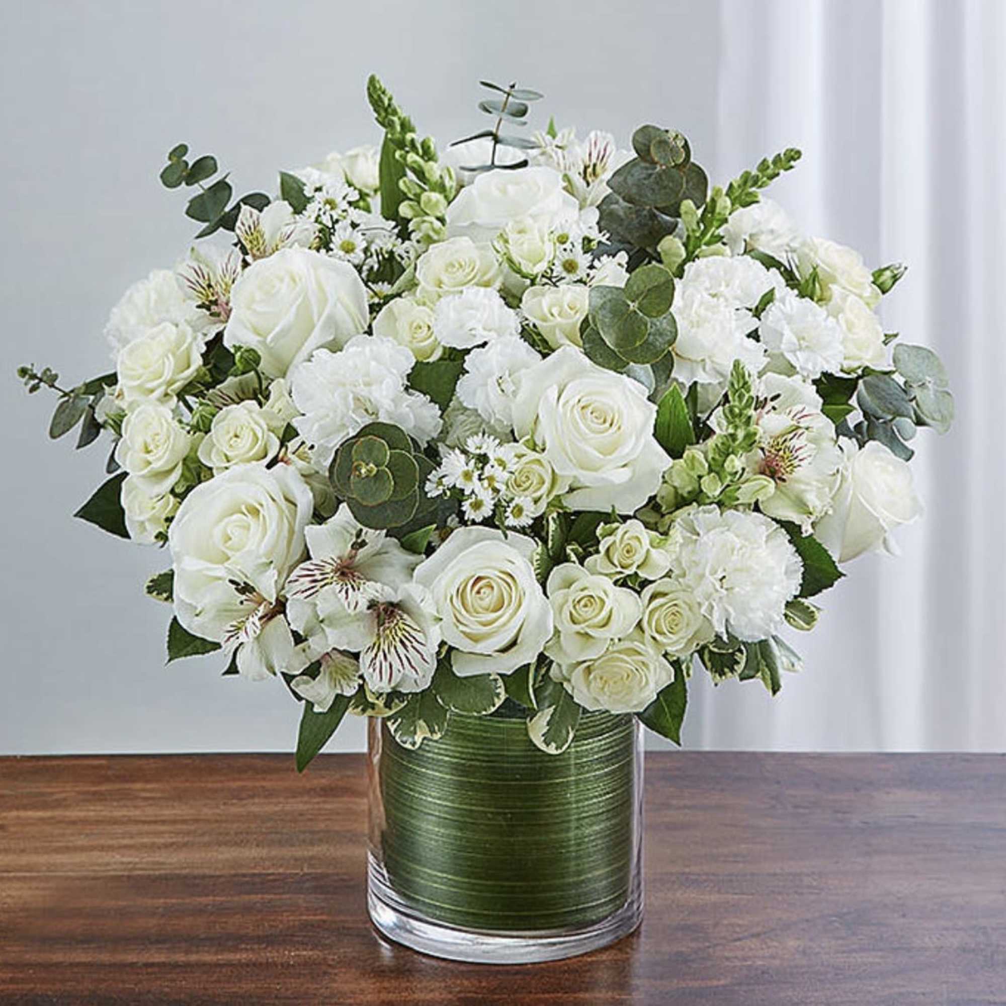 White roses and carnations in a glass vase with greenery