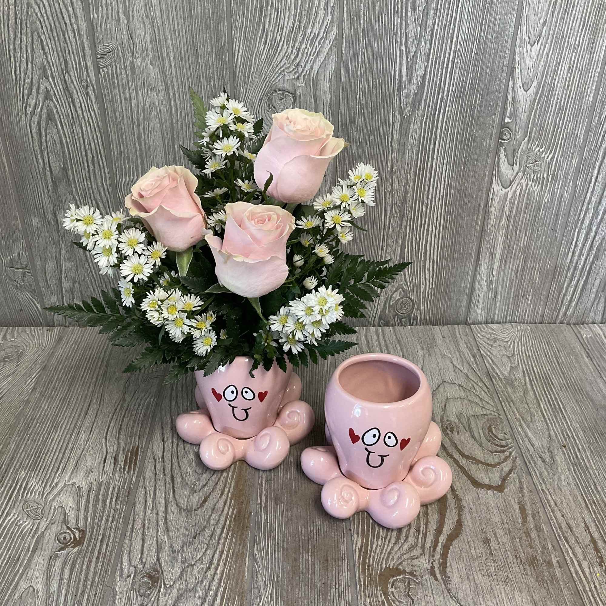 Pink roses and white daisies in a pink novelty pot with a matching empty pot beside it