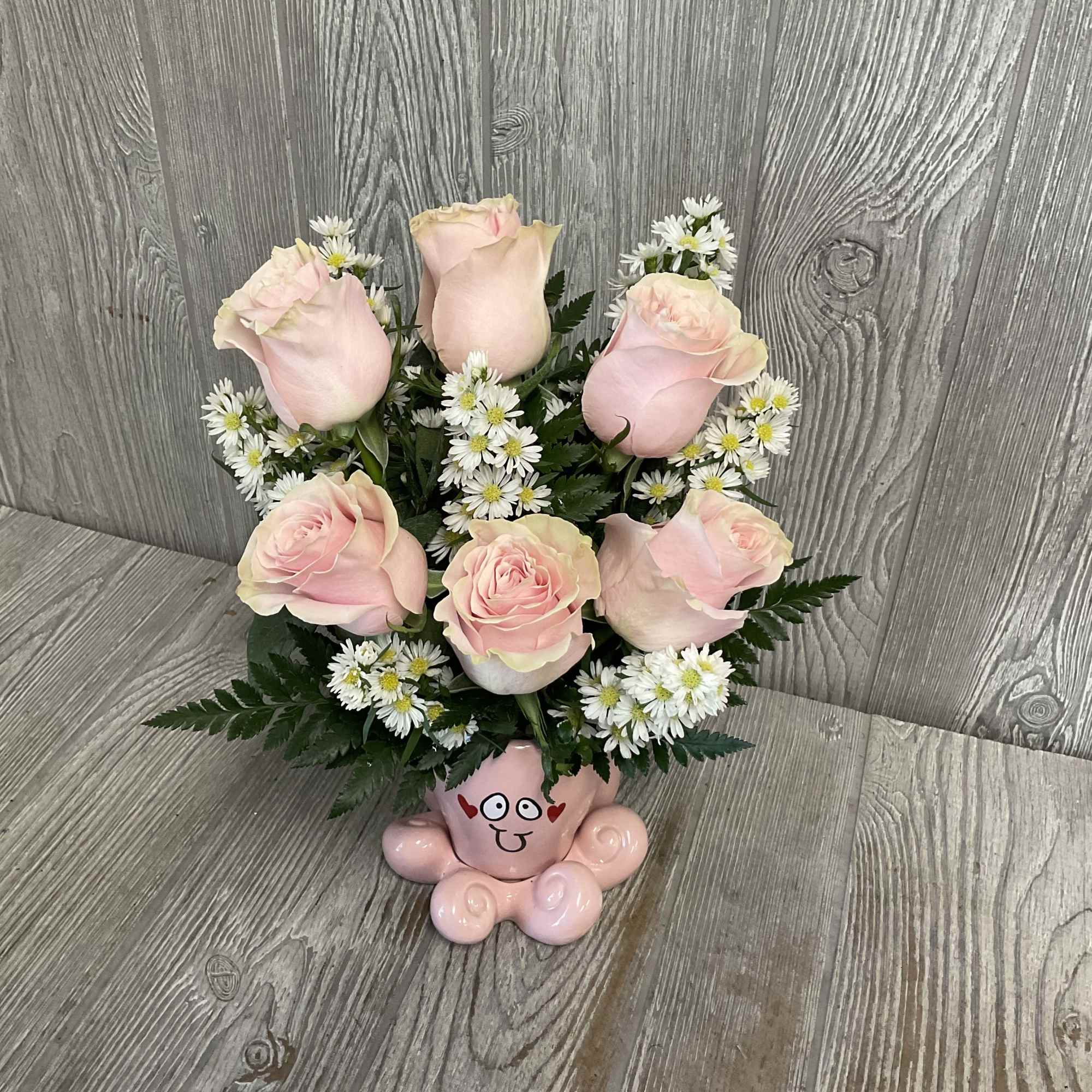 Pink roses and white daisies arranged in a pink cartoon-face vase