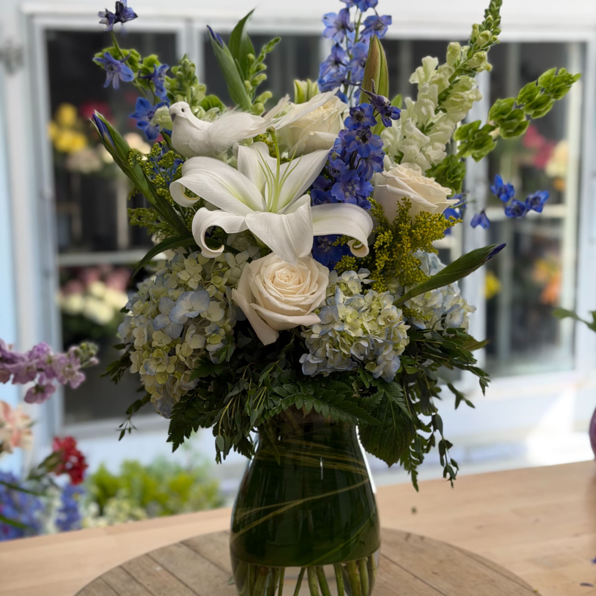 White lilies and roses with blue flowers in a glass vase