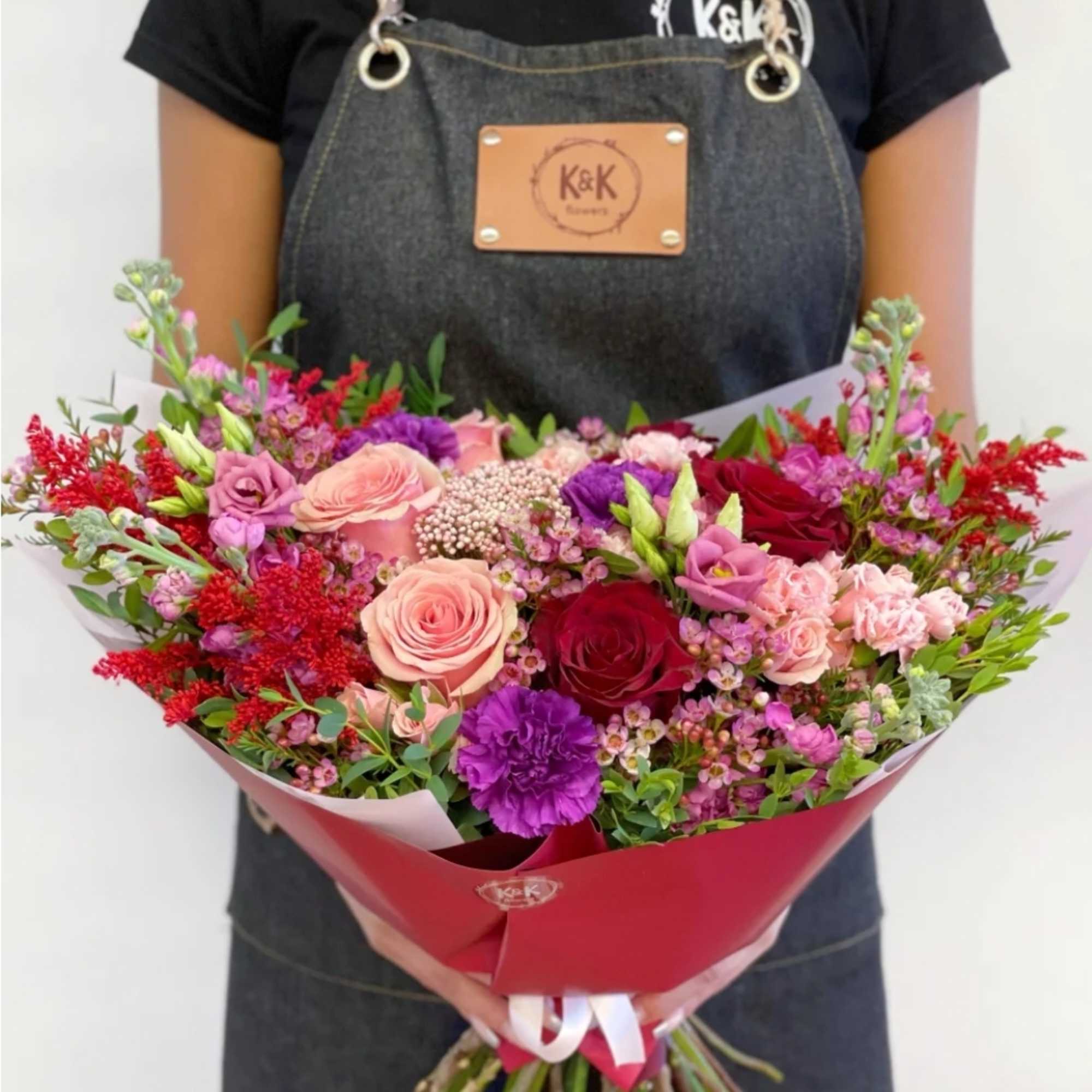 Large mixed bouquet of pink, red, and purple flowers wrapped in red paper