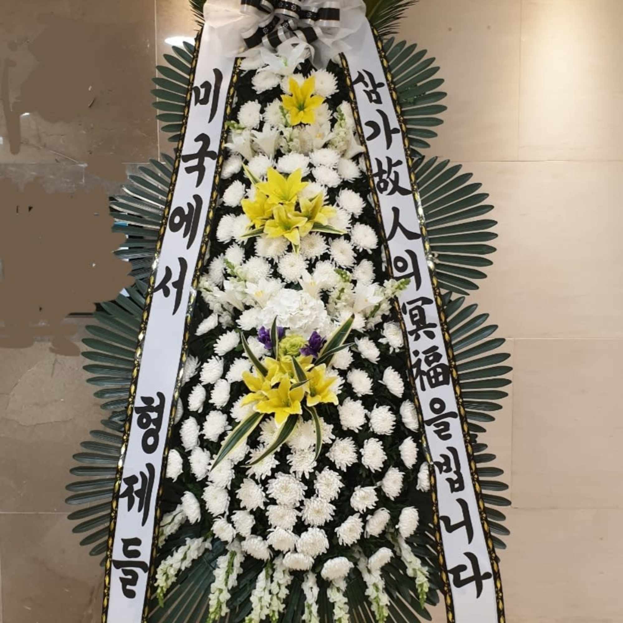 Standing funeral wreath with white and yellow flowers and Korean condolence ribbons