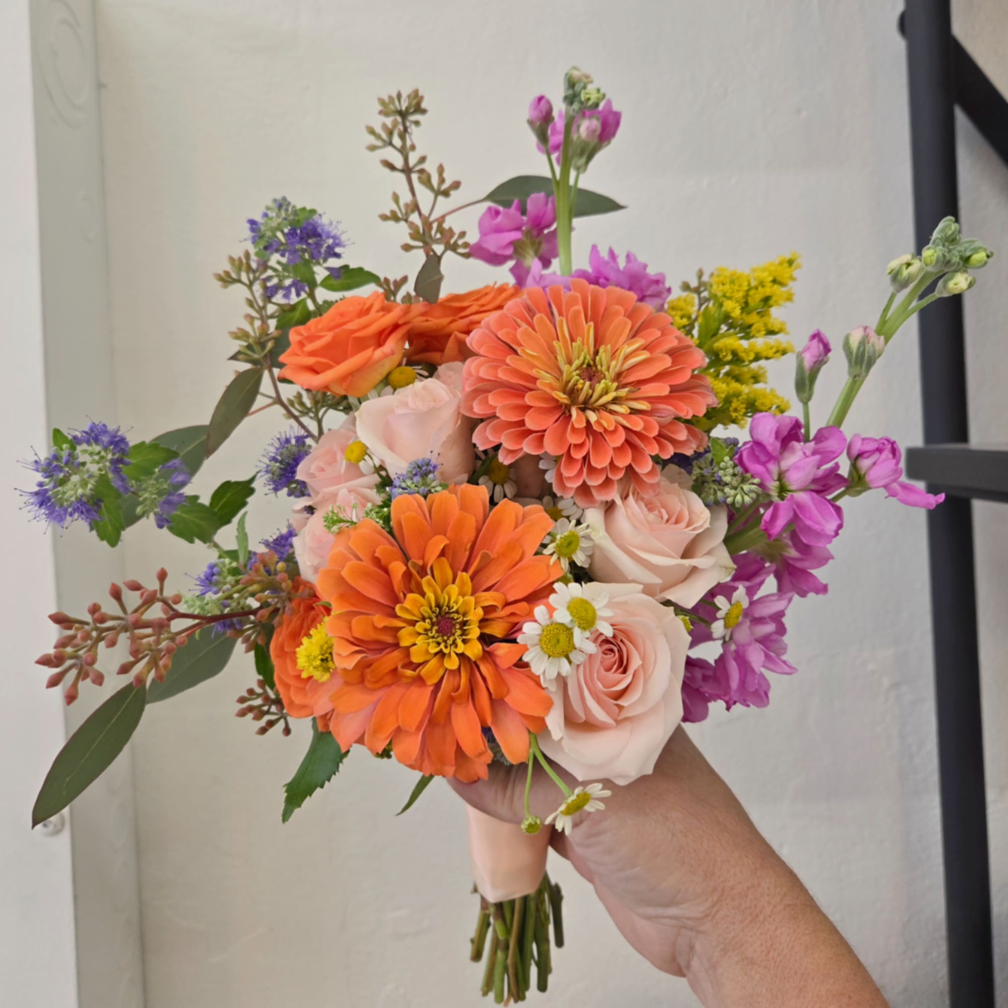 Handheld bouquet with orange zinnias, pale roses, and purple flowers