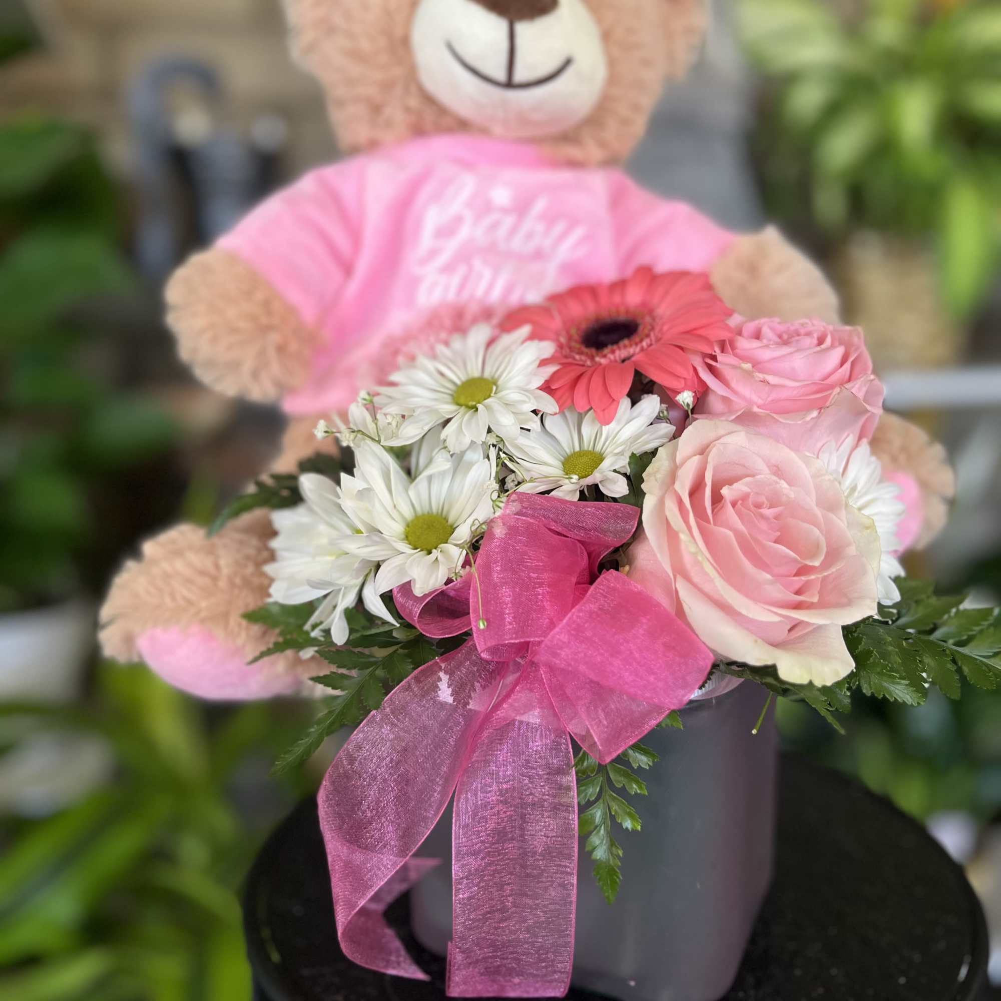 Pink teddy bear holding a bouquet of pink roses and white daisies