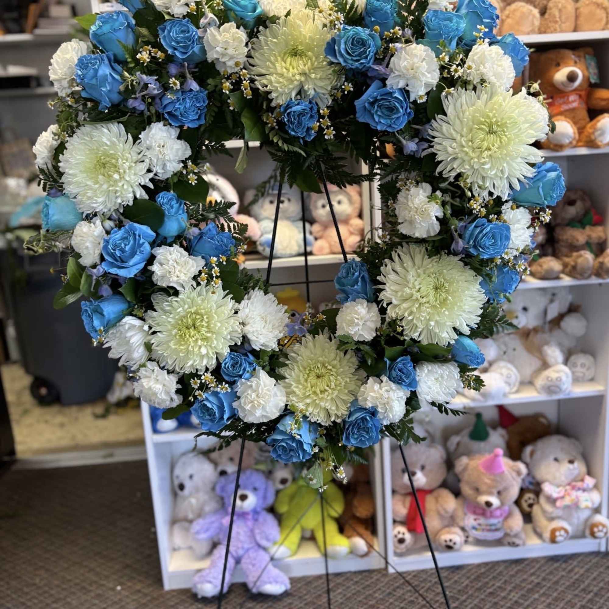 Heart-shaped floral wreath with blue roses and white chrysanthemums on a stand