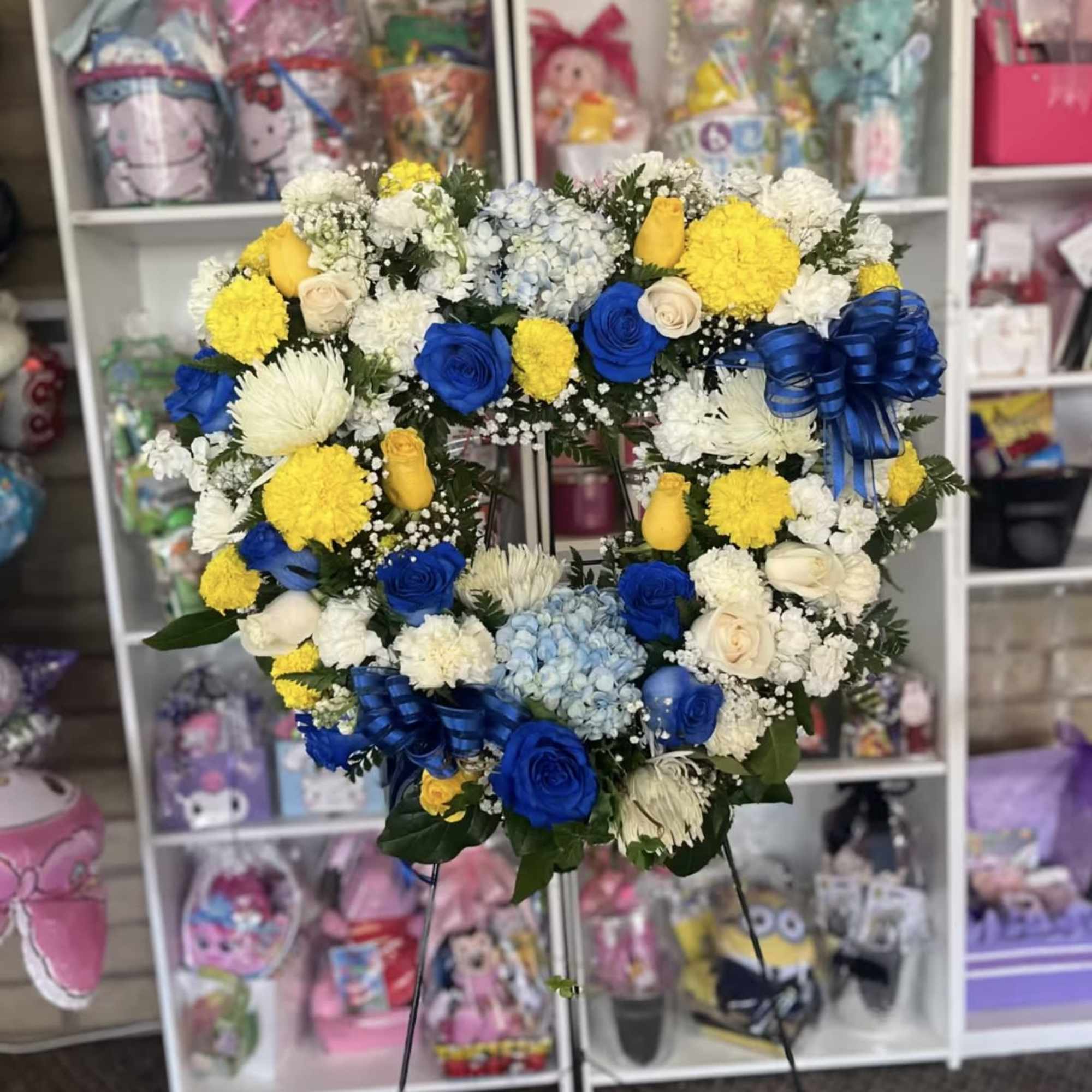 Heart-shaped floral wreath with blue, yellow, and white flowers on a stand