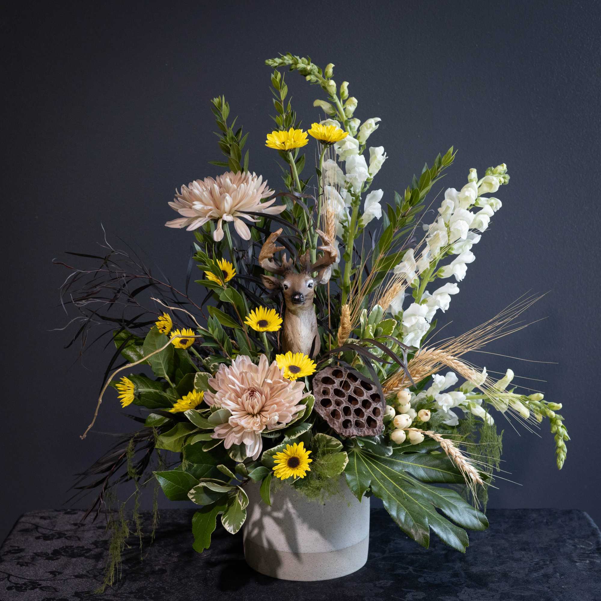 Mixed floral arrangement with yellow daisies, pale pink blooms, and a deer figurine in a vase