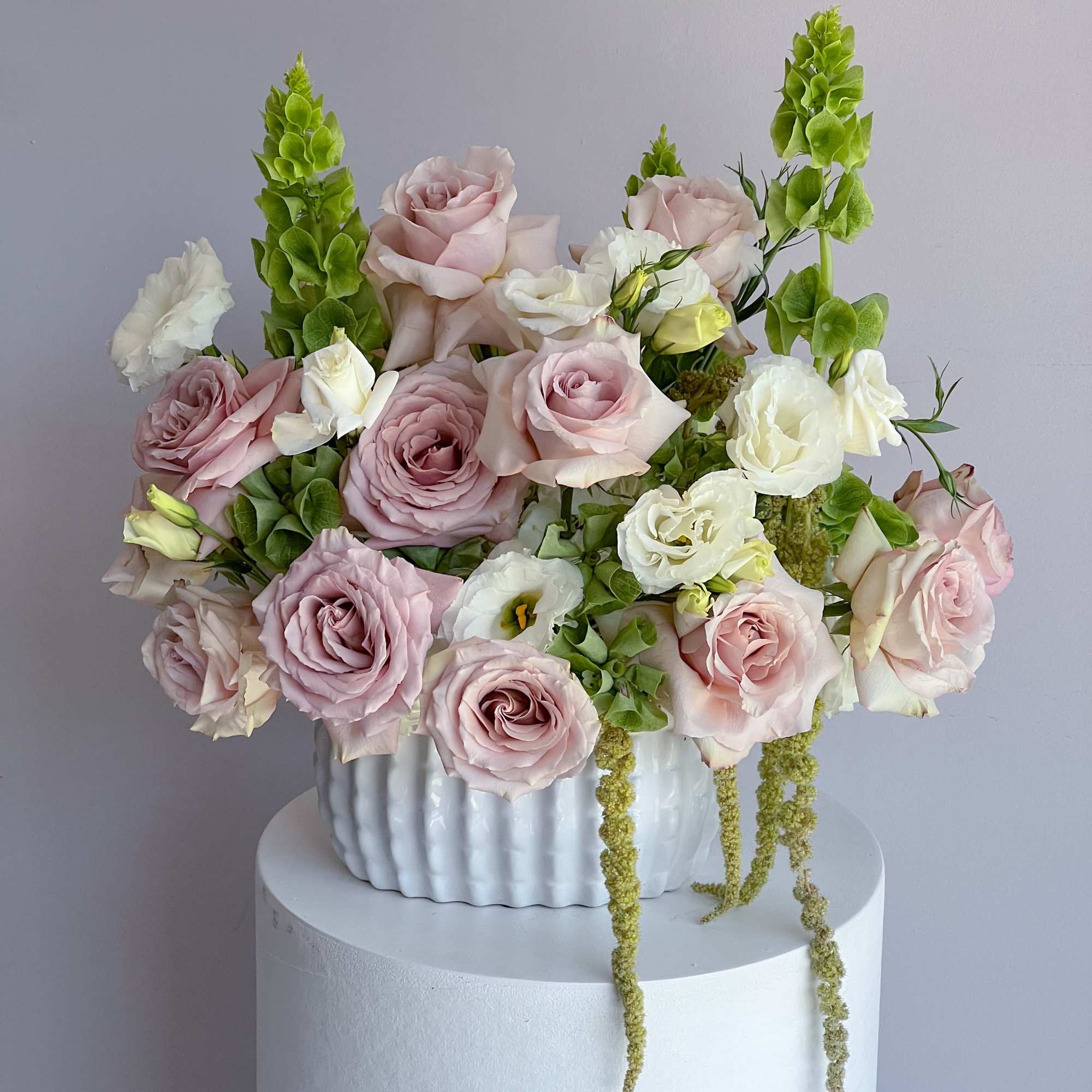 Pink and white roses arranged in a white vase with green spikes