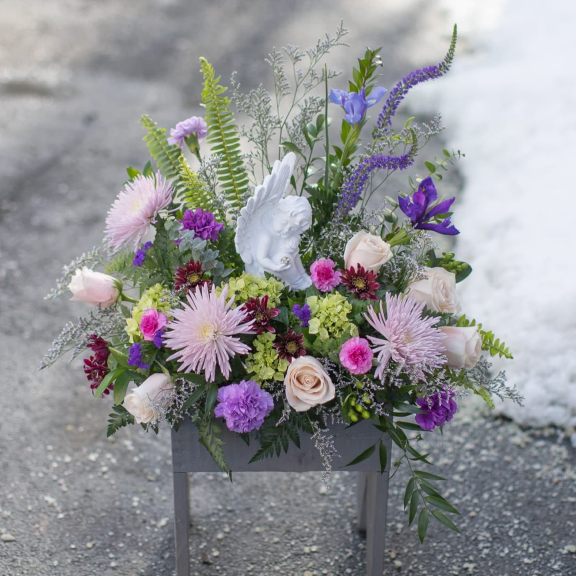 Mixed pastel floral arrangement with a white angel figurine in a gray container