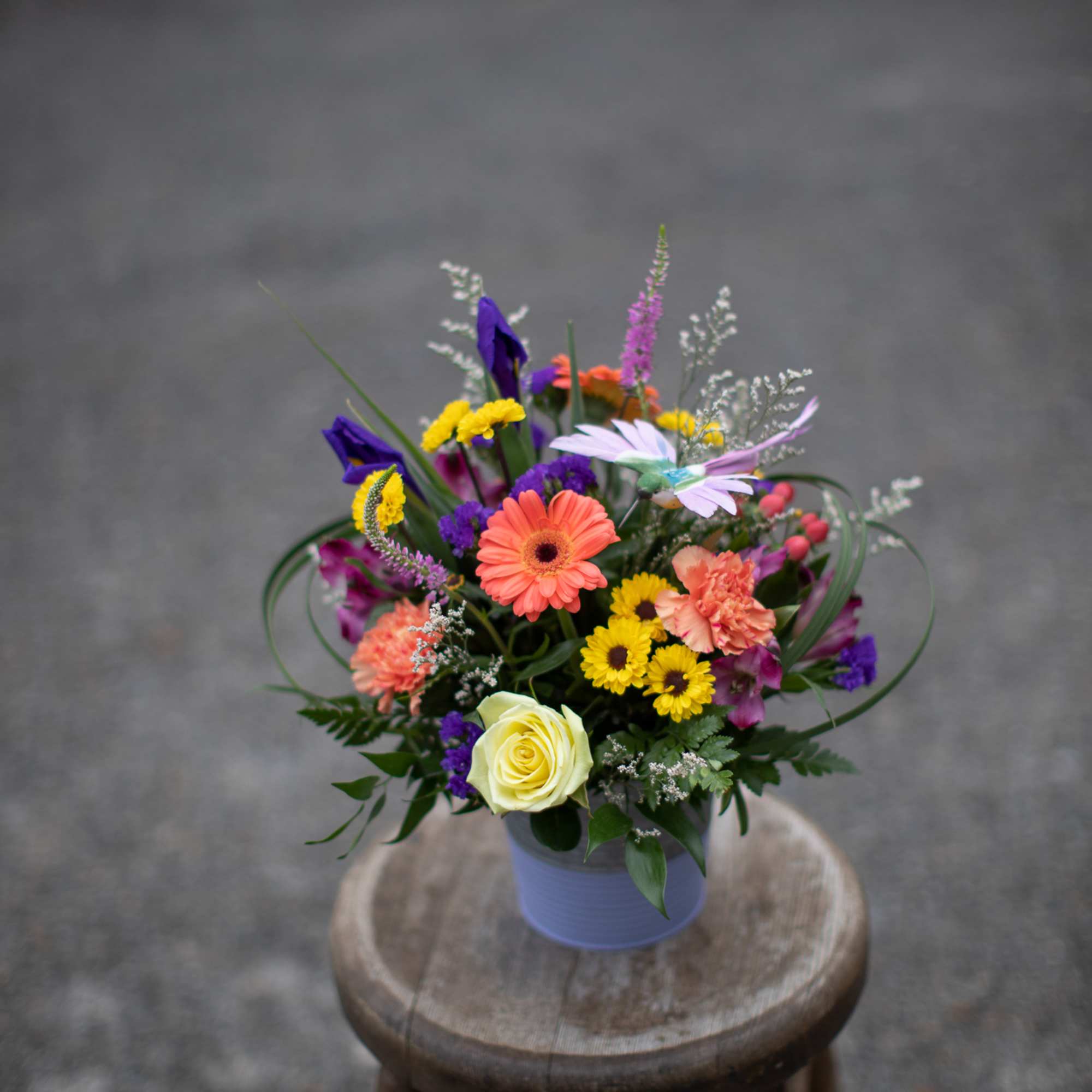 Mixed bouquet in a lavender vase with bright pink, yellow, purple, and white flowers