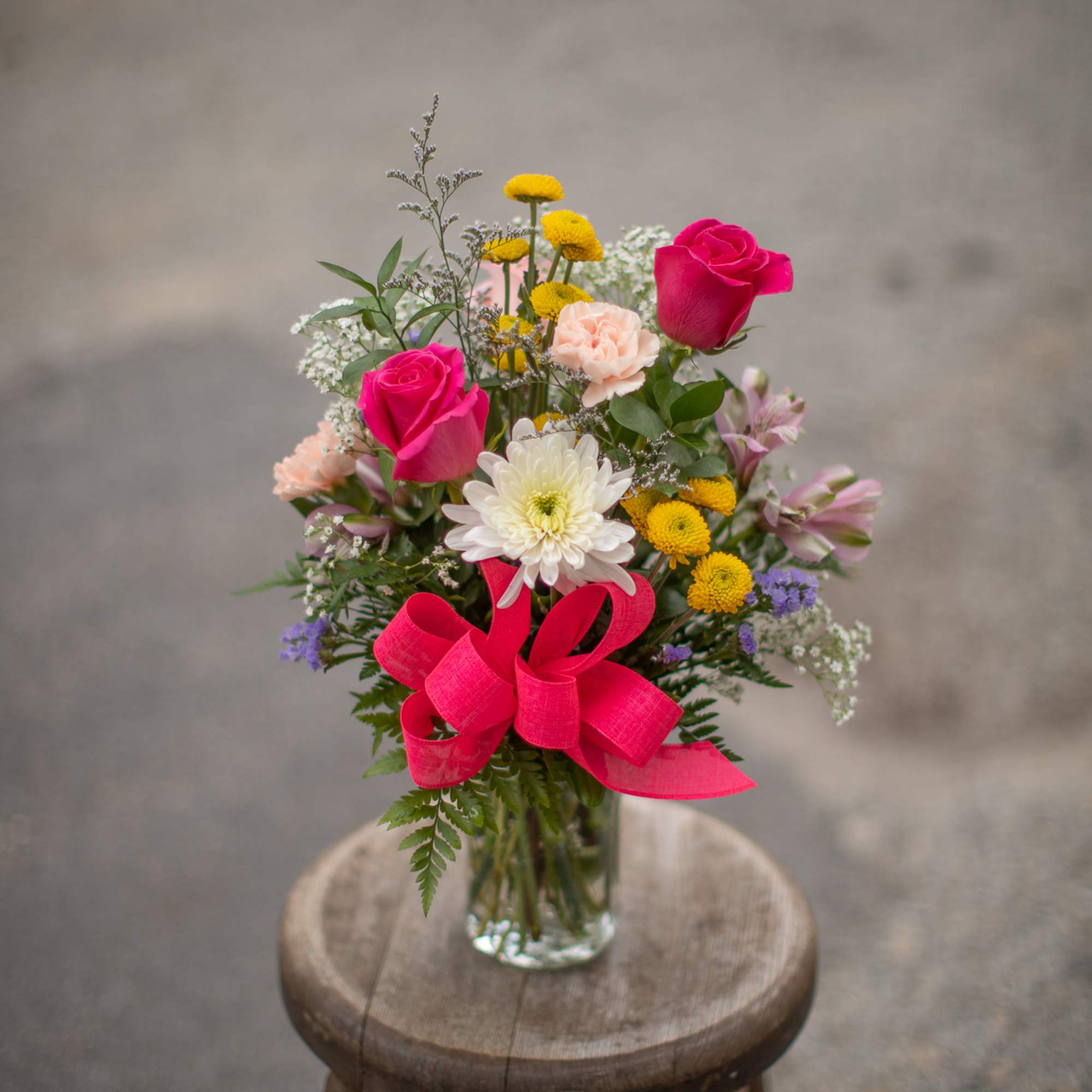 Mixed bouquet of pink roses, white daisy-like blooms, and yellow flowers in a glass vase