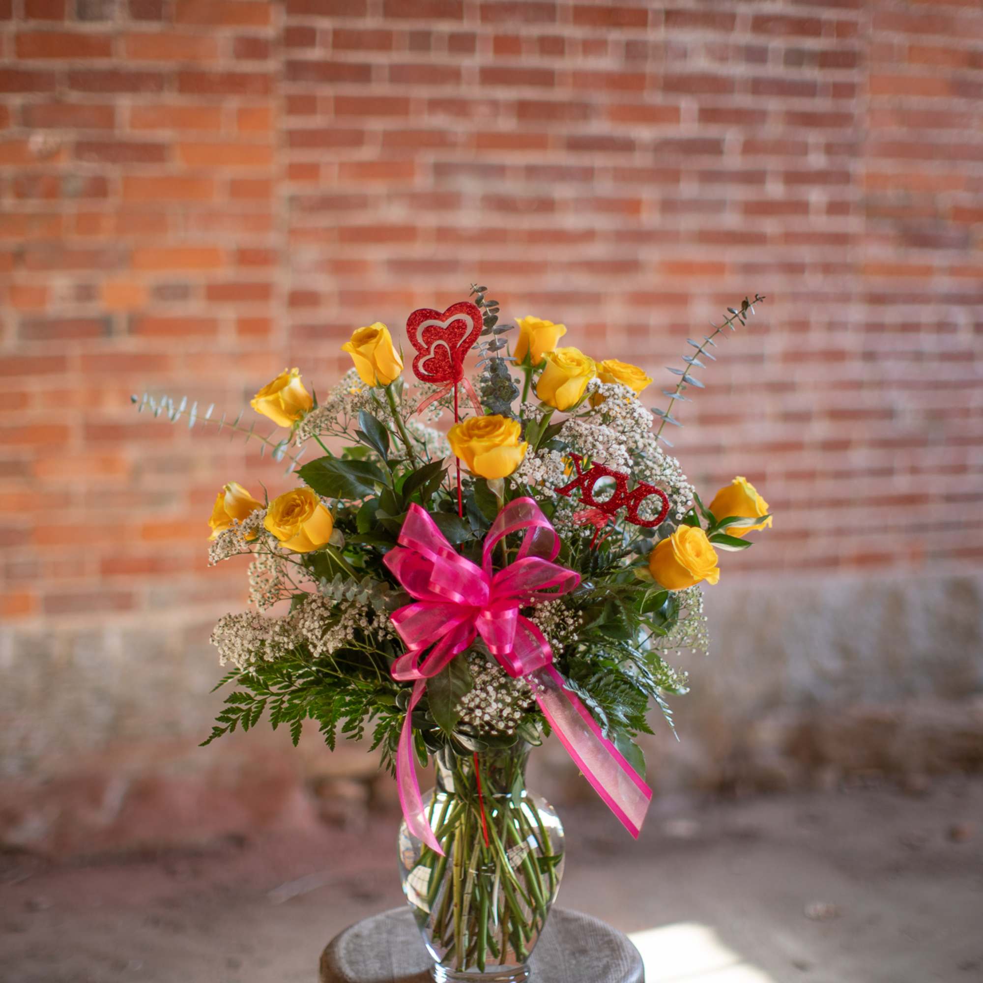 Yellow roses in a glass vase with pink ribbon and heart picks