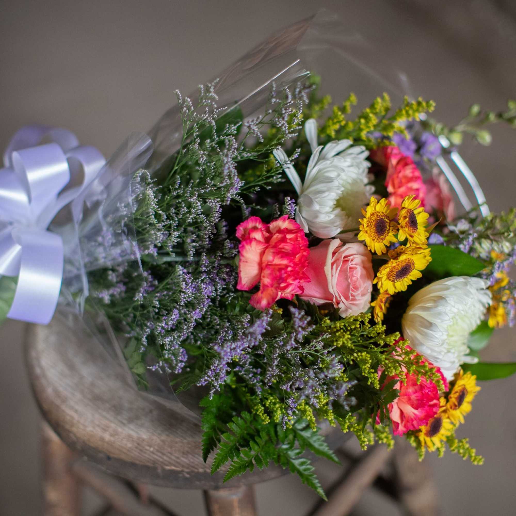 Bouquet of mixed flowers wrapped in clear plastic with a white ribbon
