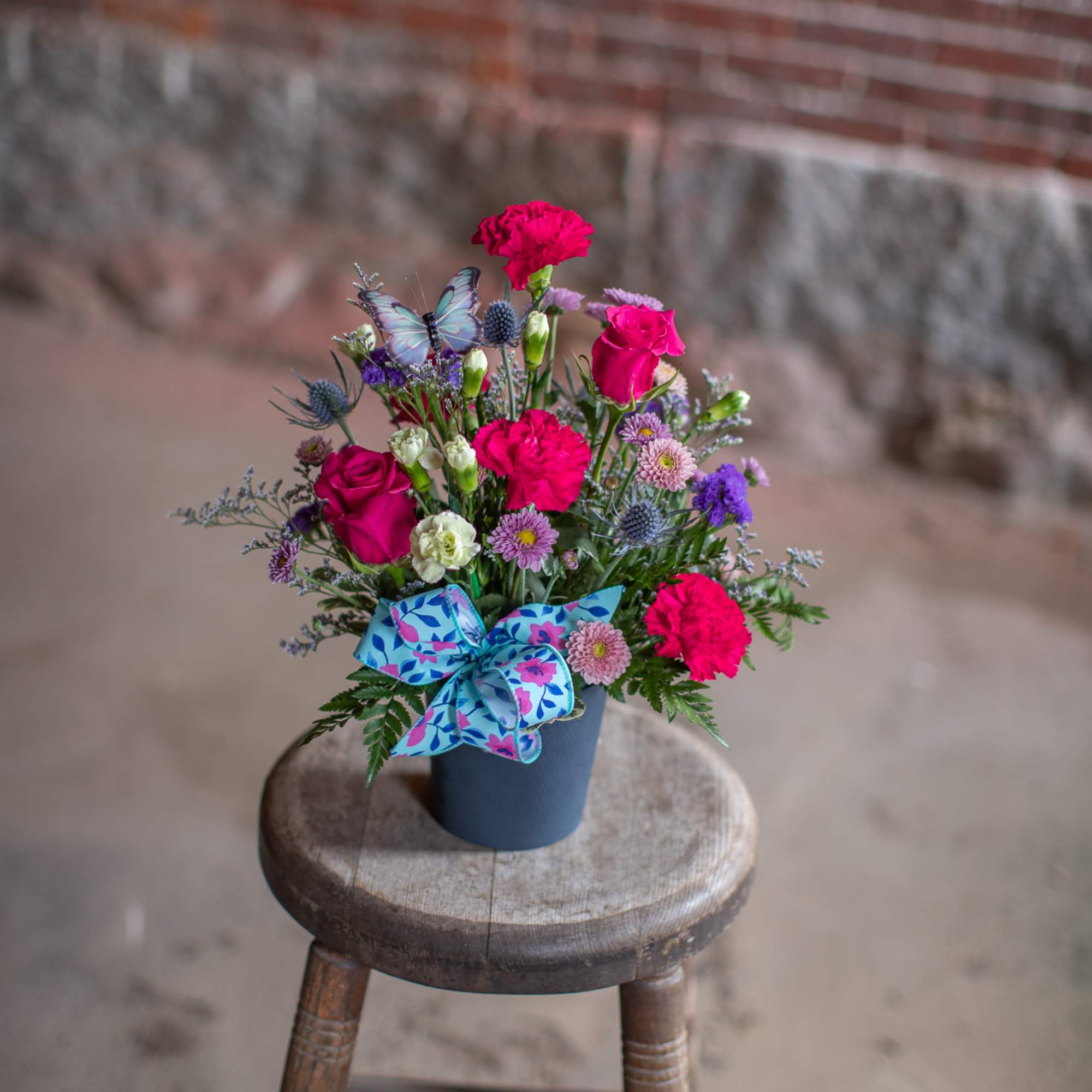 Bright mixed bouquet in a blue container with a decorative ribbon
