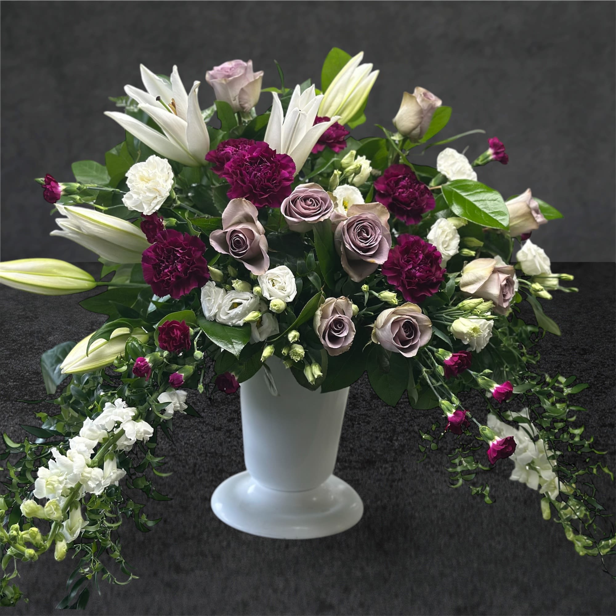 White lilies and mauve roses in a white pedestal vase
