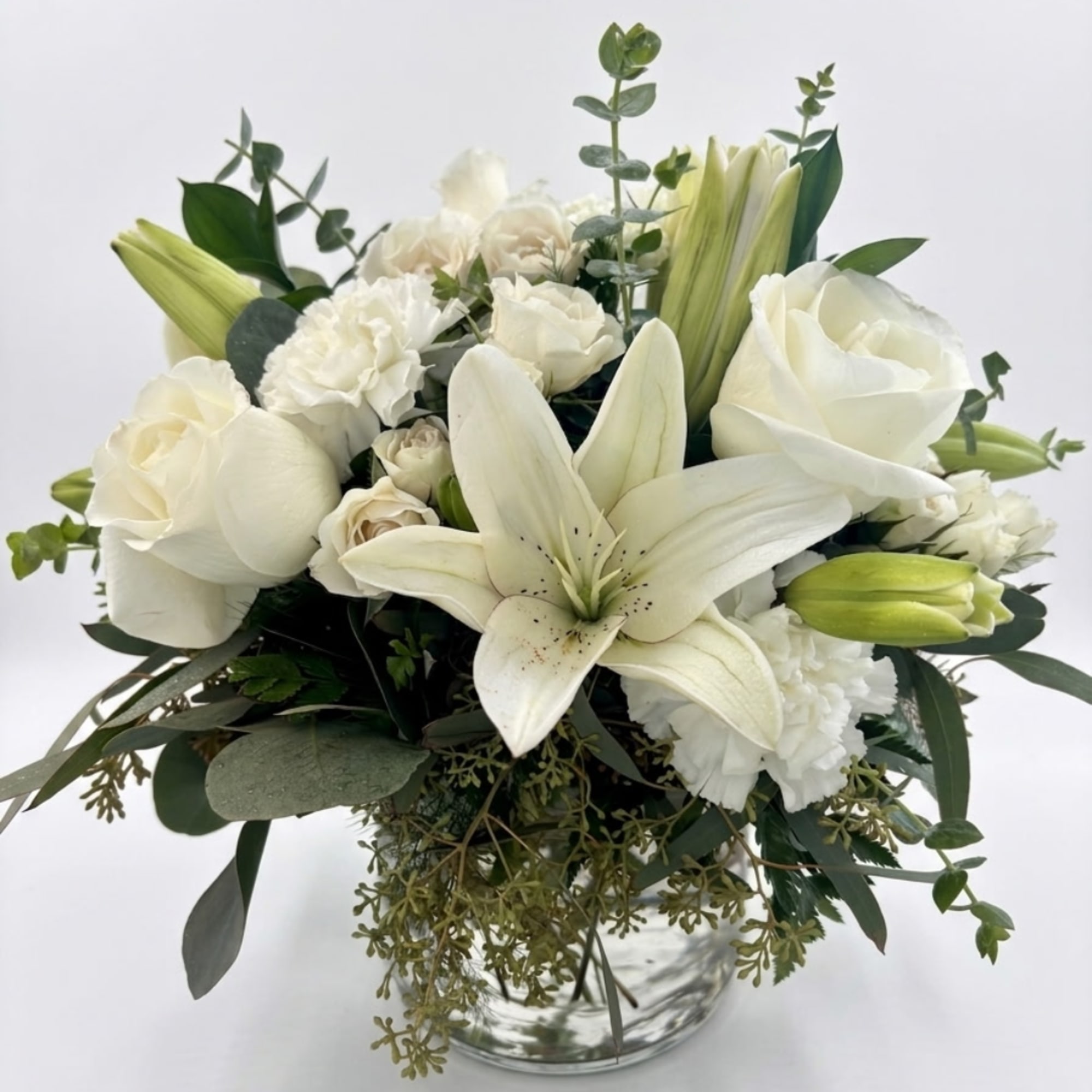 White lilies and roses arranged in a clear glass vase