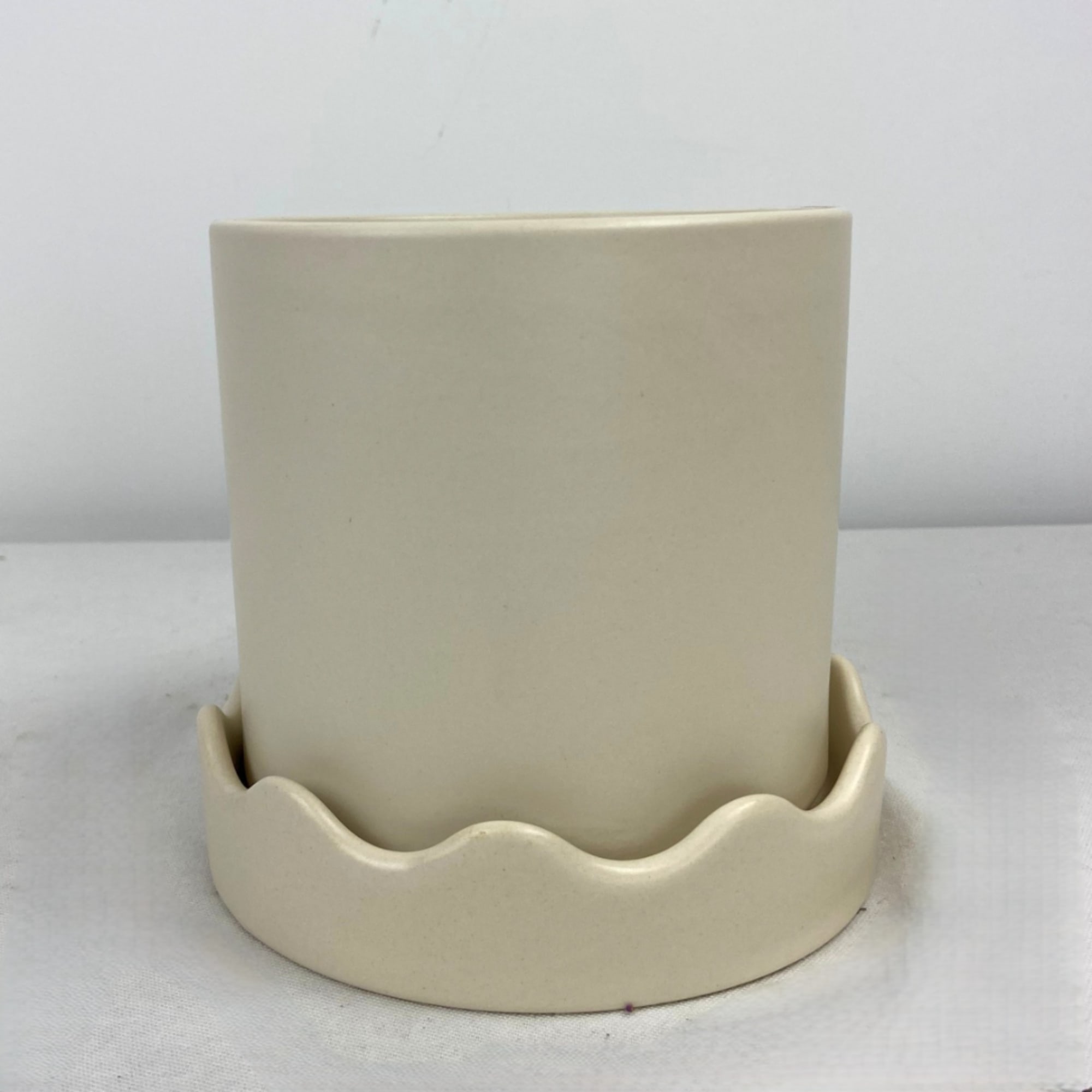 Cream ceramic planter with a scalloped base on a white surface