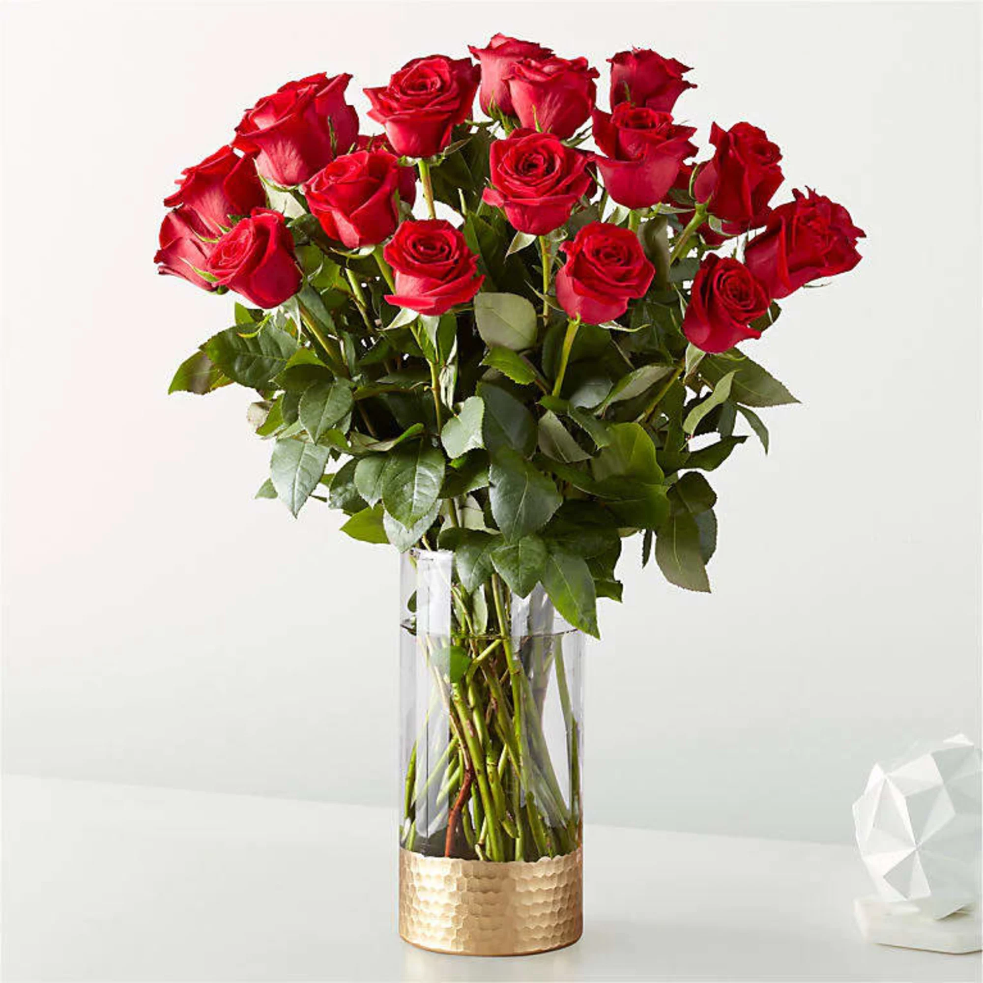 Tall bouquet of red roses in a clear glass vase with a gold base