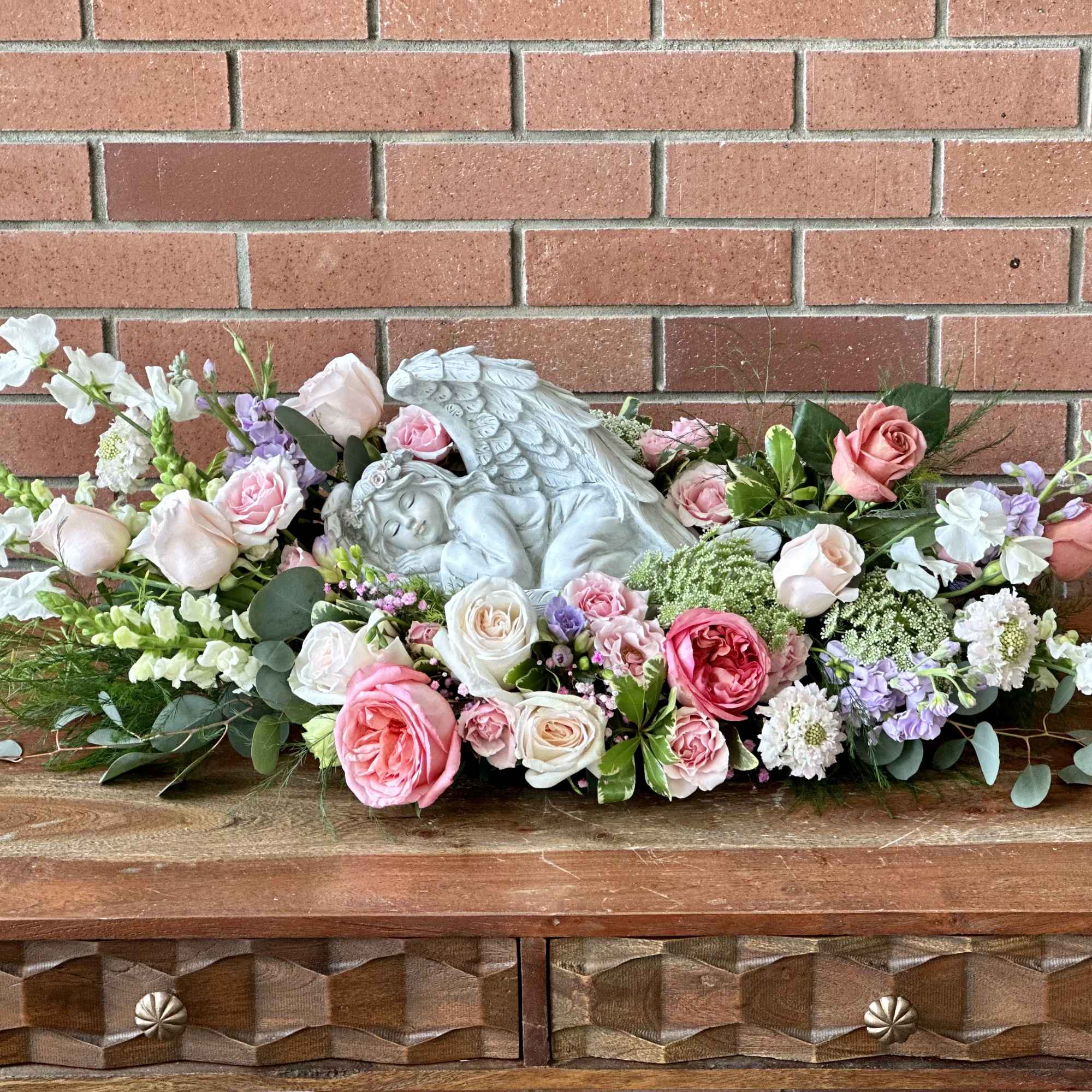 Pink and white rose arrangement with a sleeping angel statue