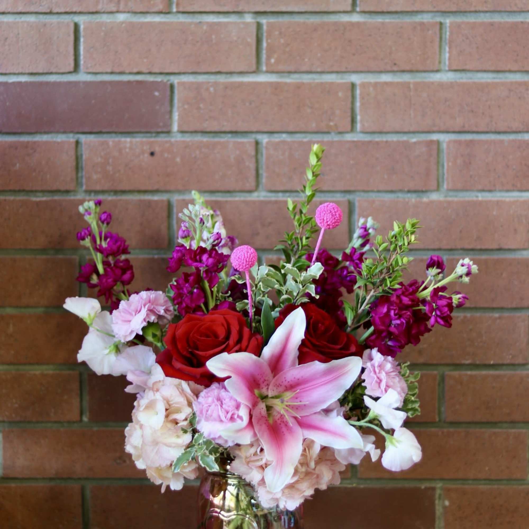 Bouquet of red roses, pink lily, and magenta flowers in a glass vase