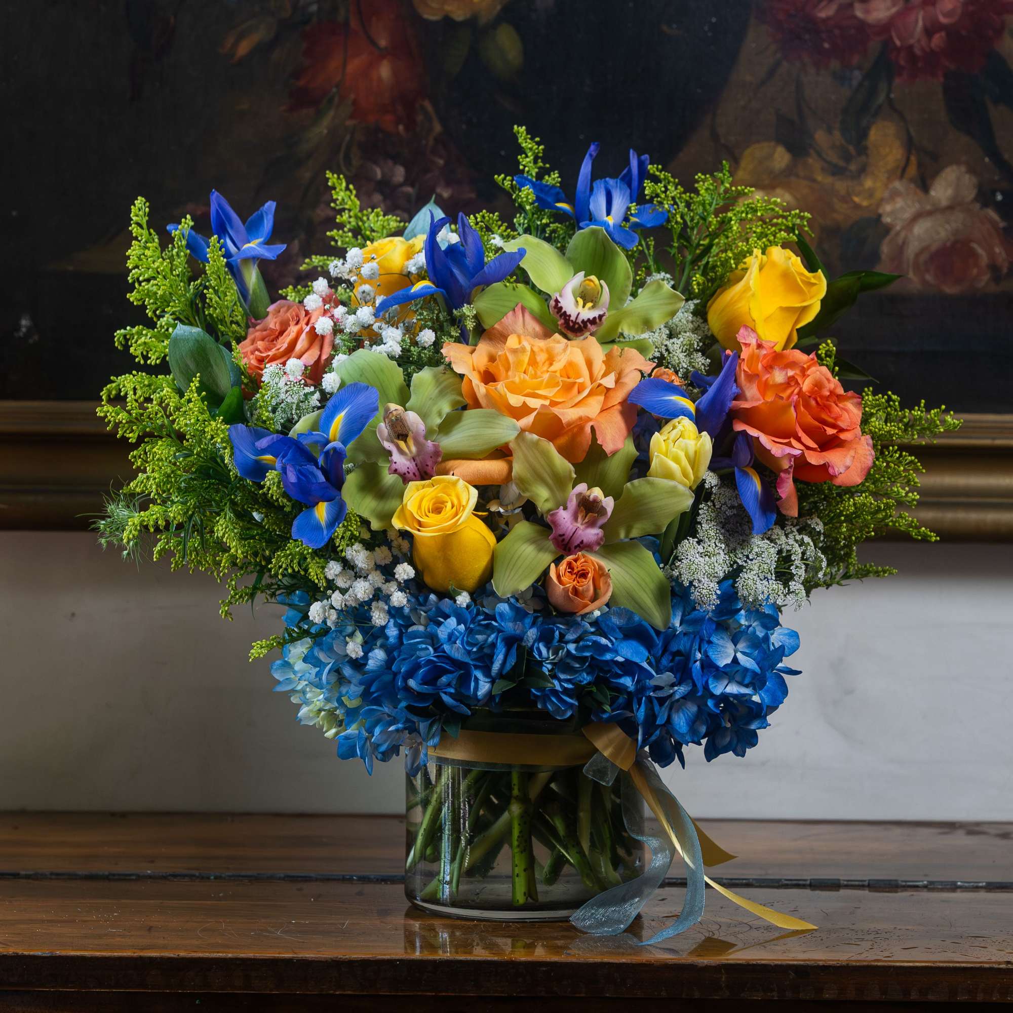 Arranged with Summer flowers including orange roses, yellow spray roses, blue hydrangeas