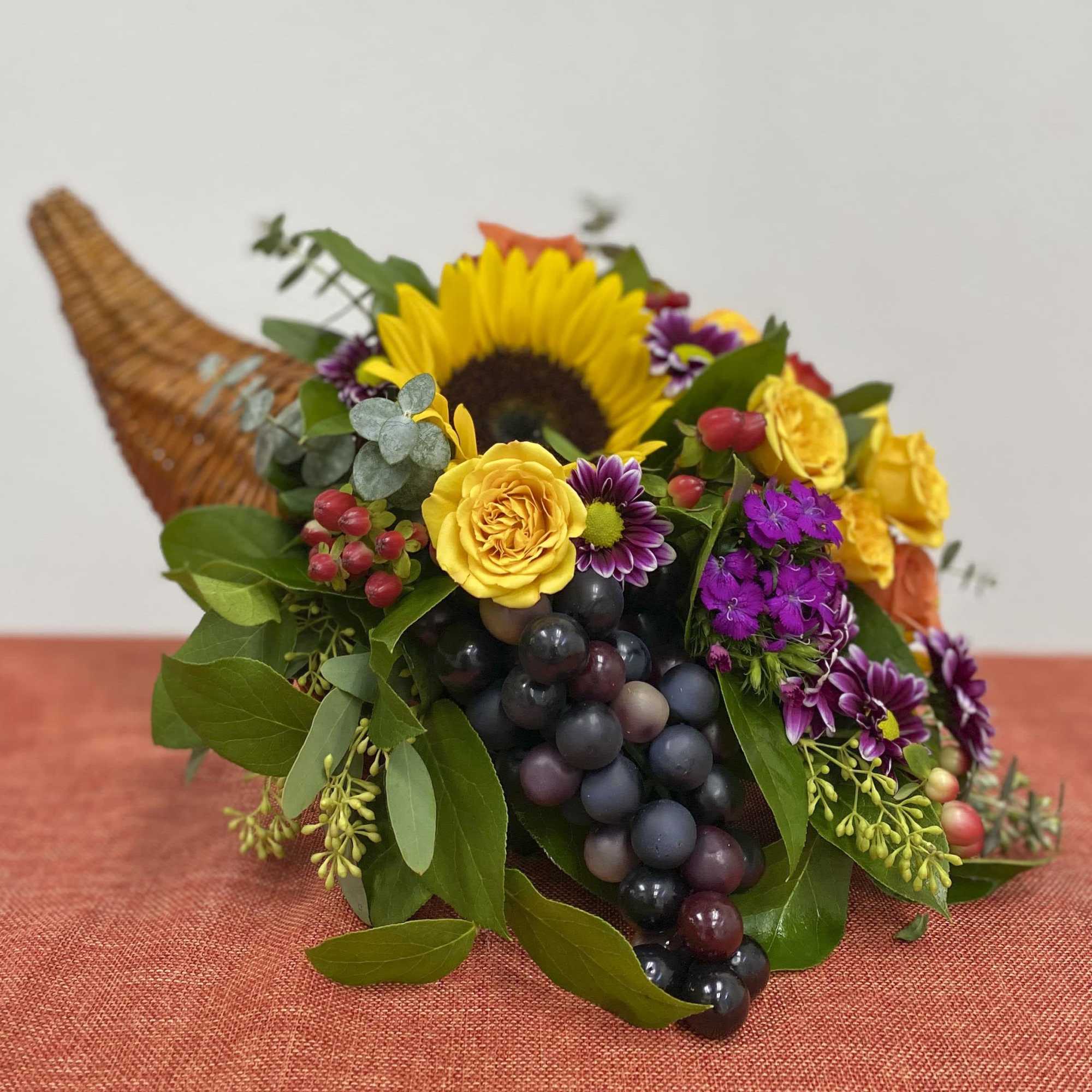 Cornucopia-style bouquet with yellow roses, sunflowers, purple flowers, and grapes