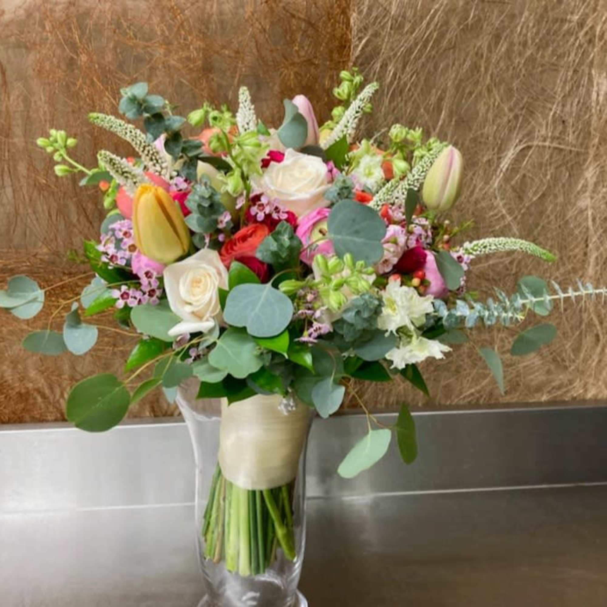 Mixed bouquet of roses, tulips, and lilies in a clear glass vase