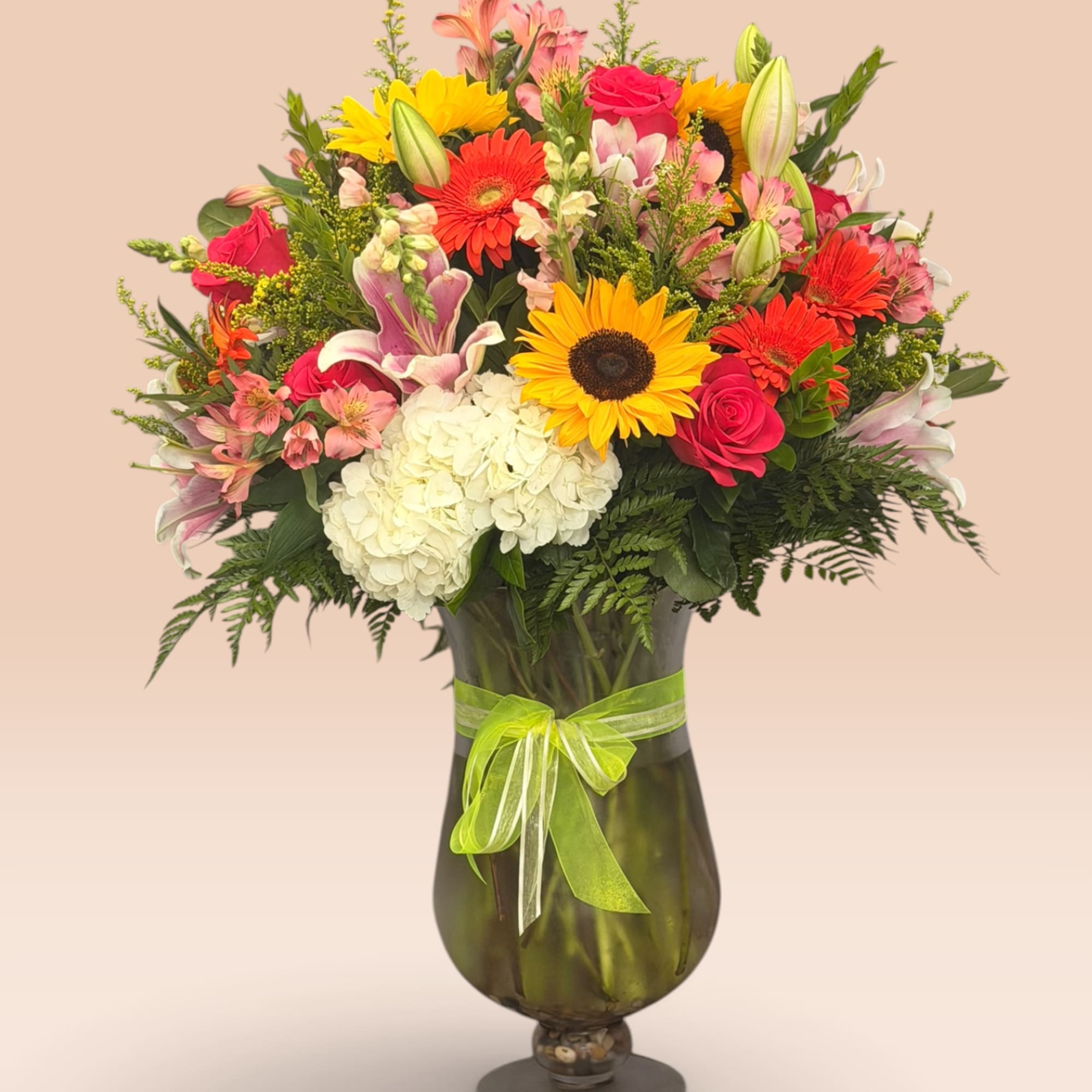 Mixed bouquet of sunflowers, roses, lilies, and hydrangea in a glass vase