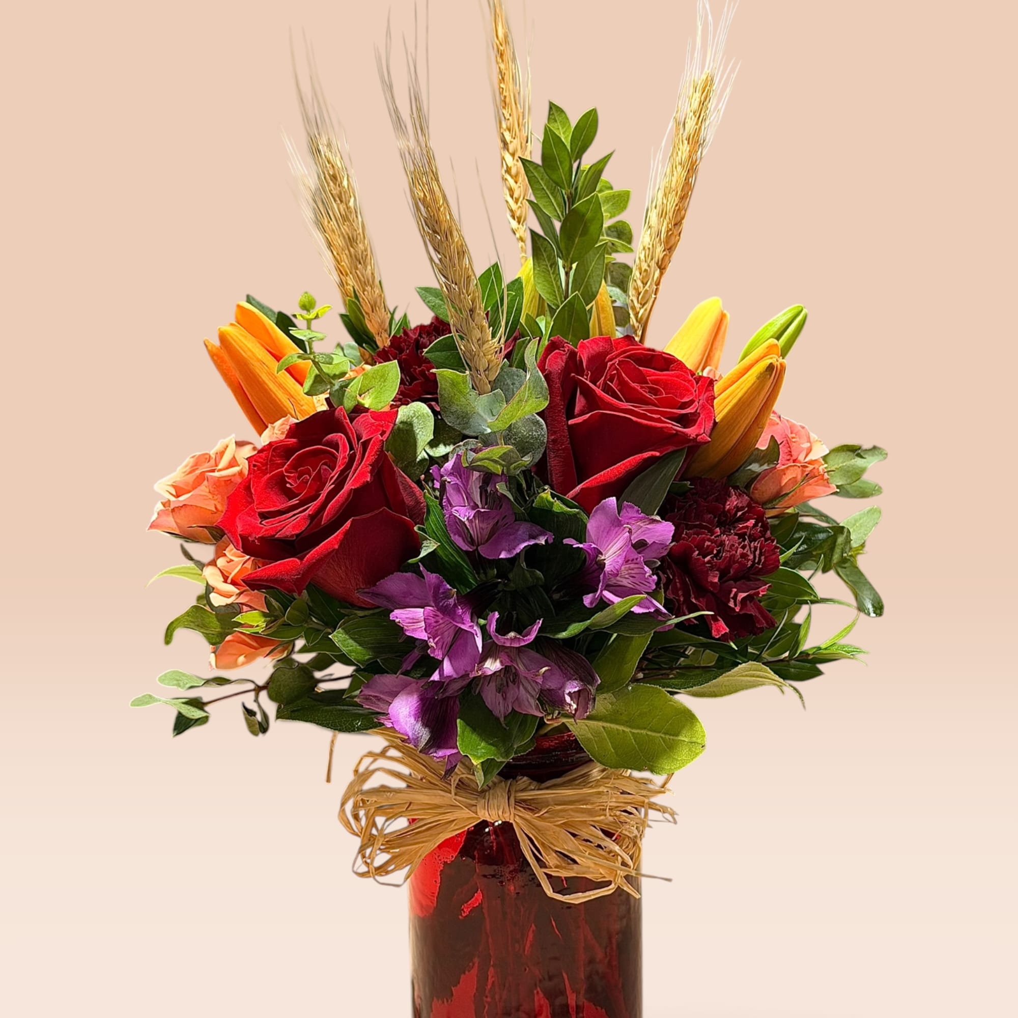 Red roses and purple flowers in a red glass vase with wheat stems