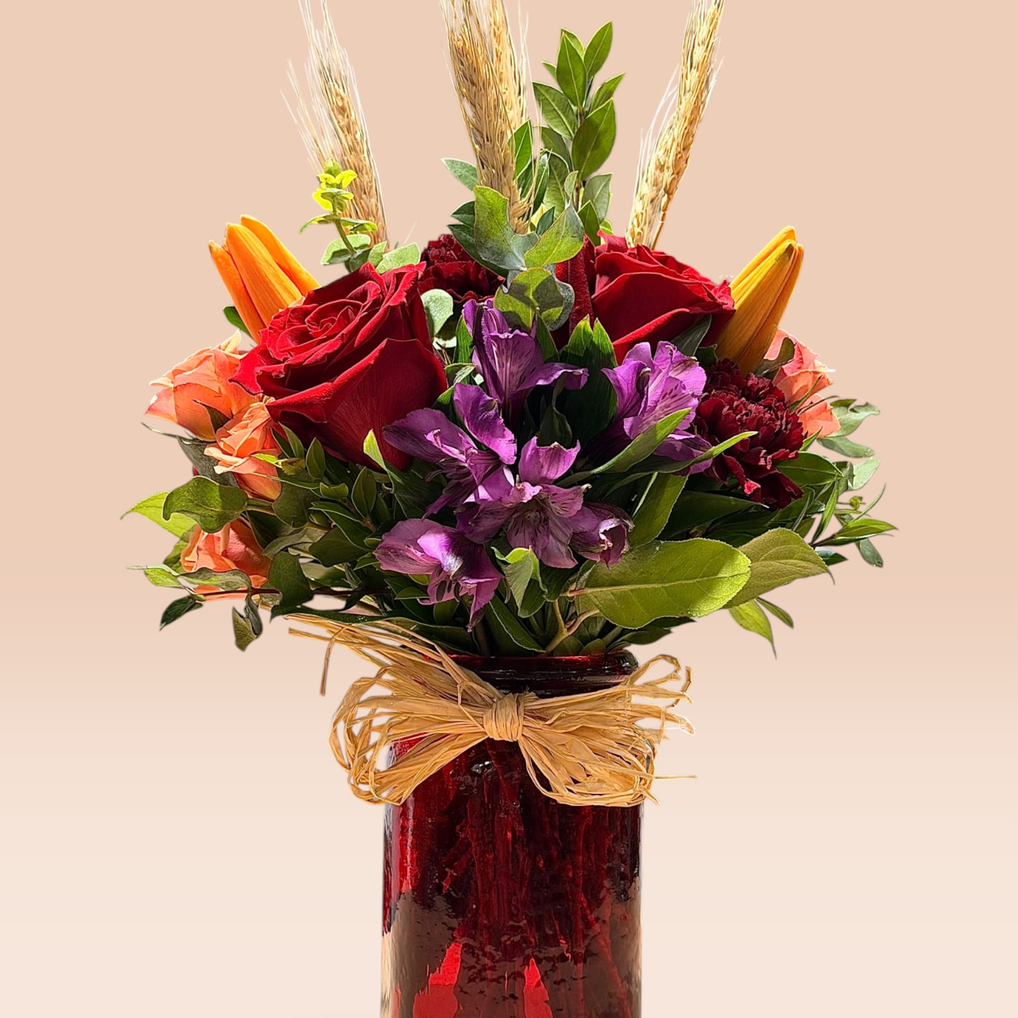 Red roses and purple flowers in a red glass vase with a raffia bow