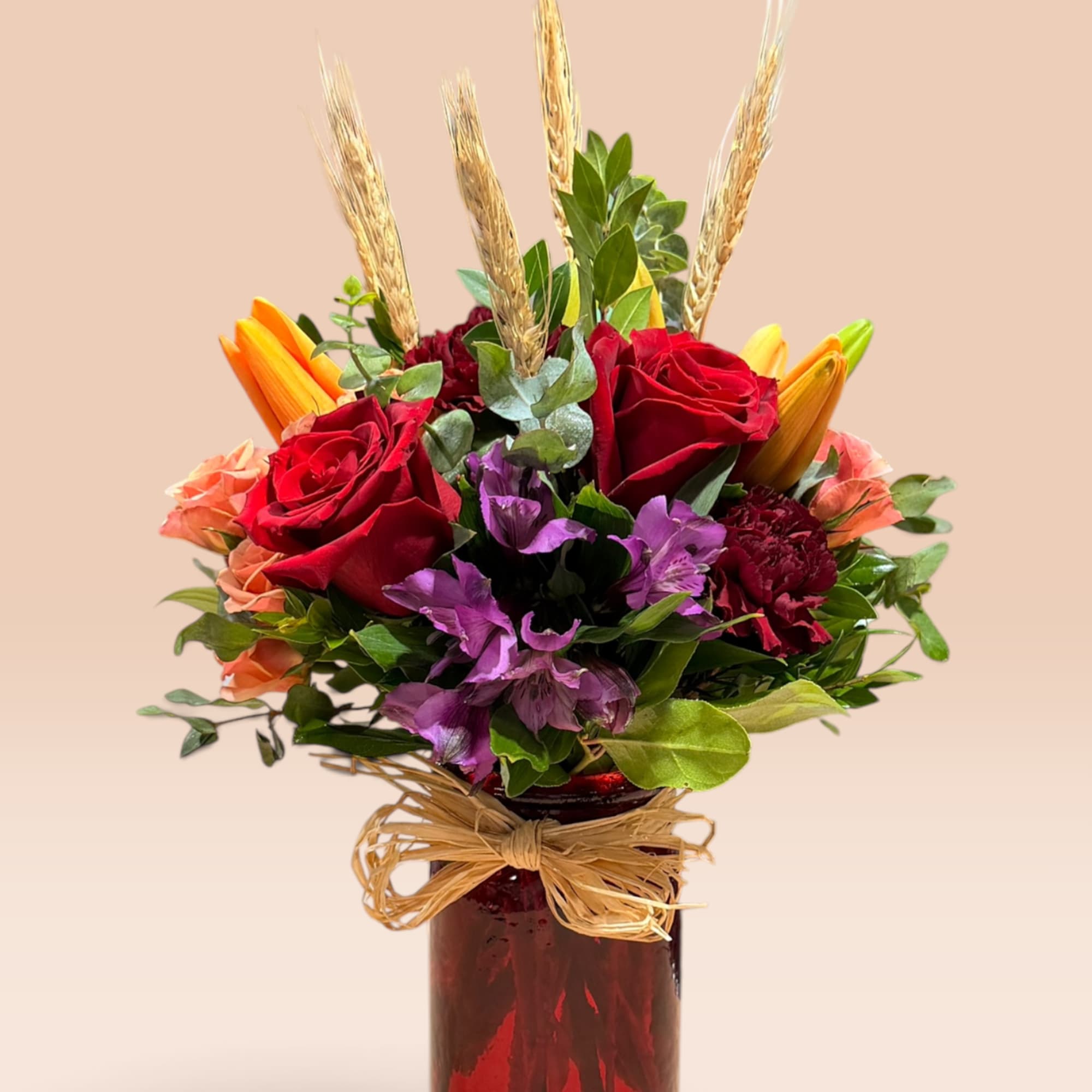 Bouquet of red roses, purple flowers, and wheat in a red glass vase