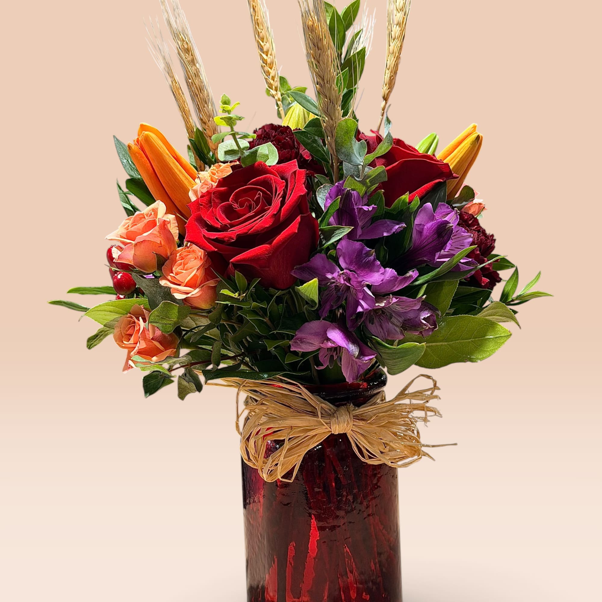 Bouquet of red roses, purple flowers, and orange blooms in a red glass vase
