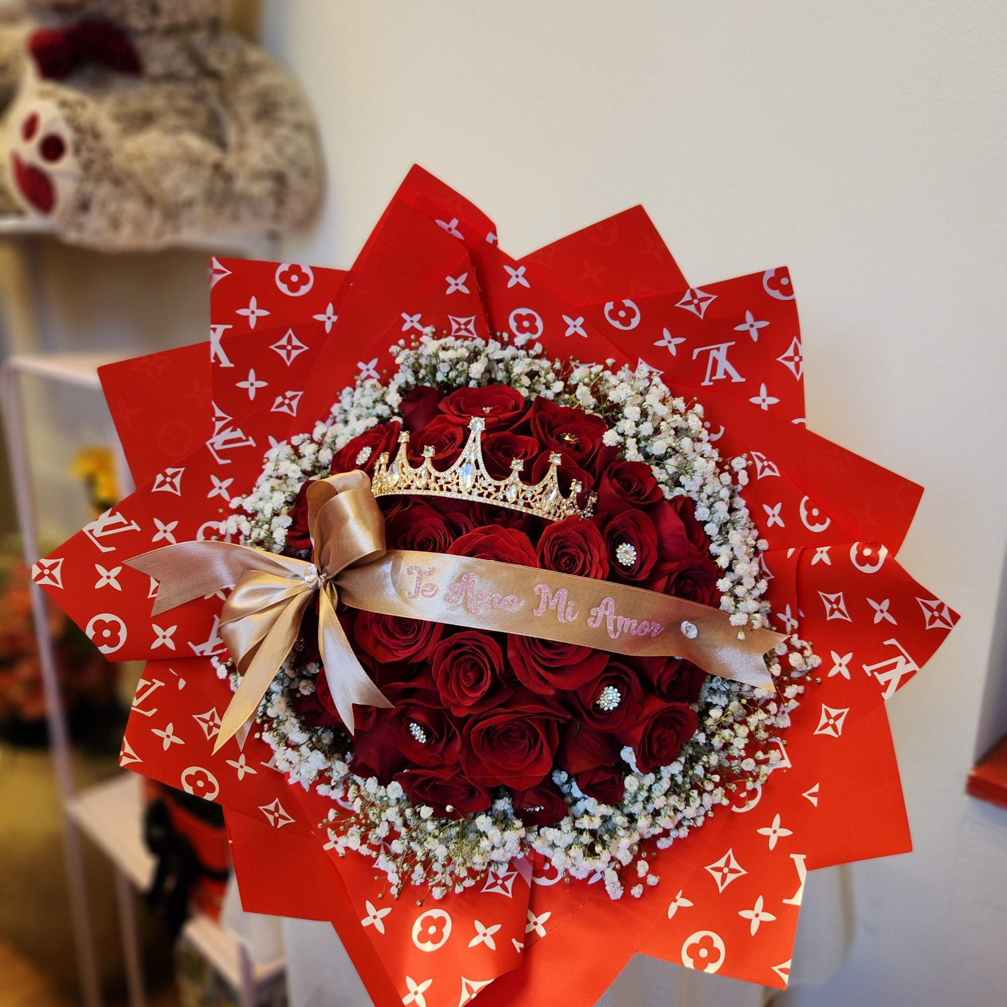 Bouquet of red roses with baby's breath, a gold ribbon, and a crown topper