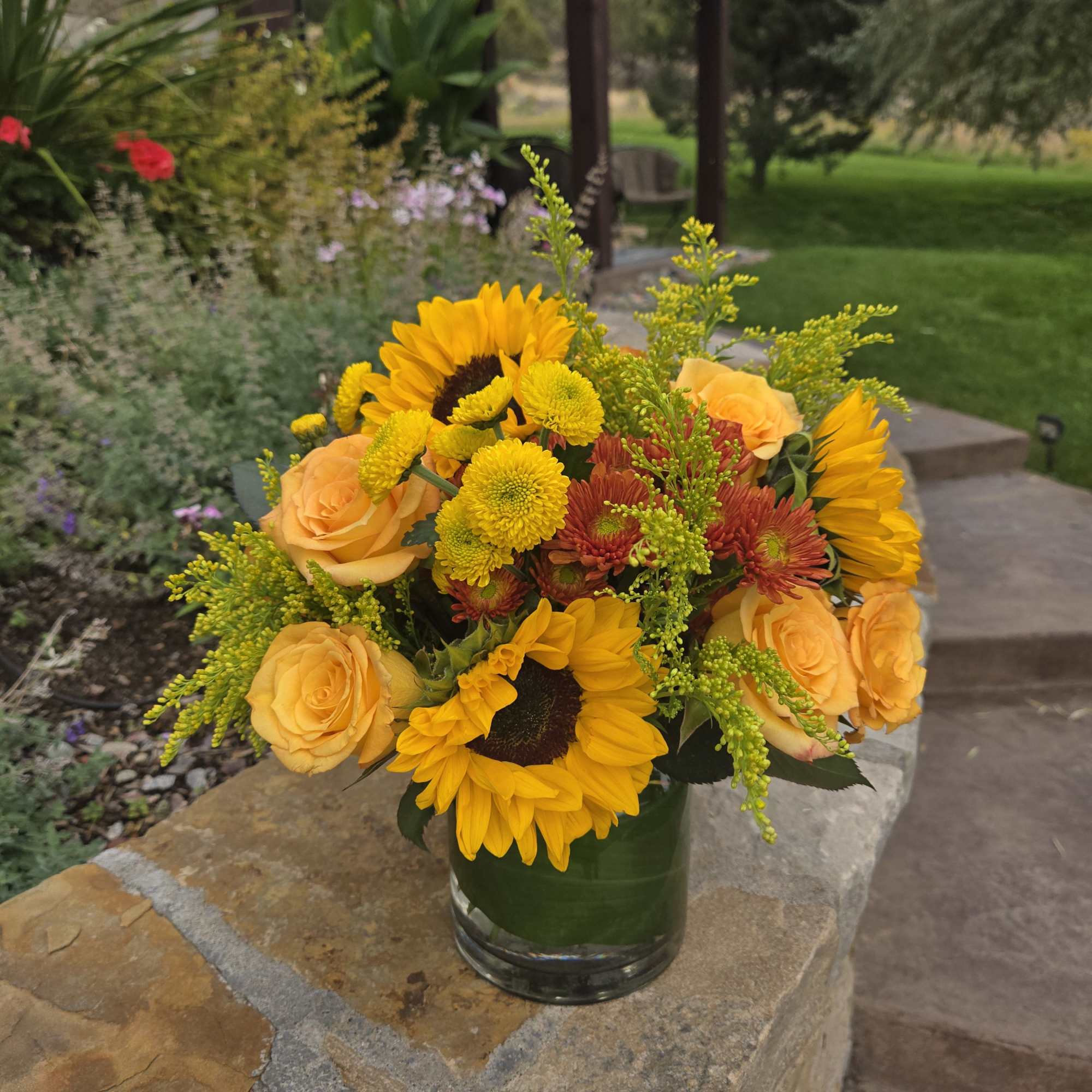 Bouquet of sunflowers, yellow roses, and mums in a glass vase