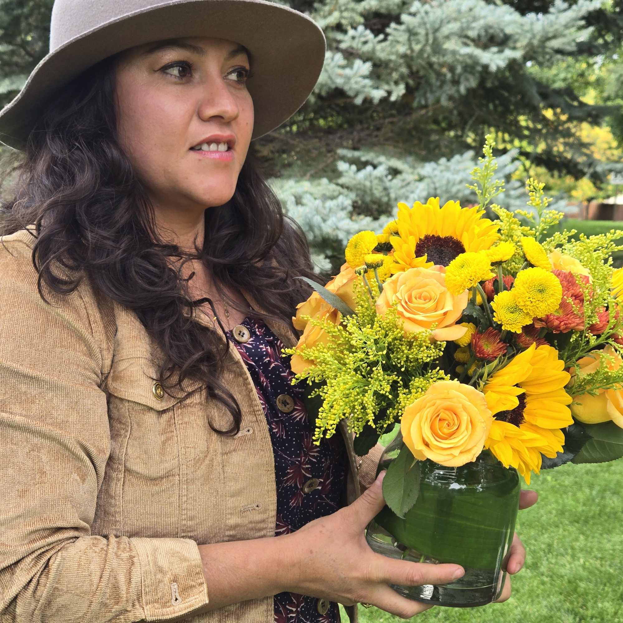 Woman holding a yellow and orange flower arrangement in a glass vase
