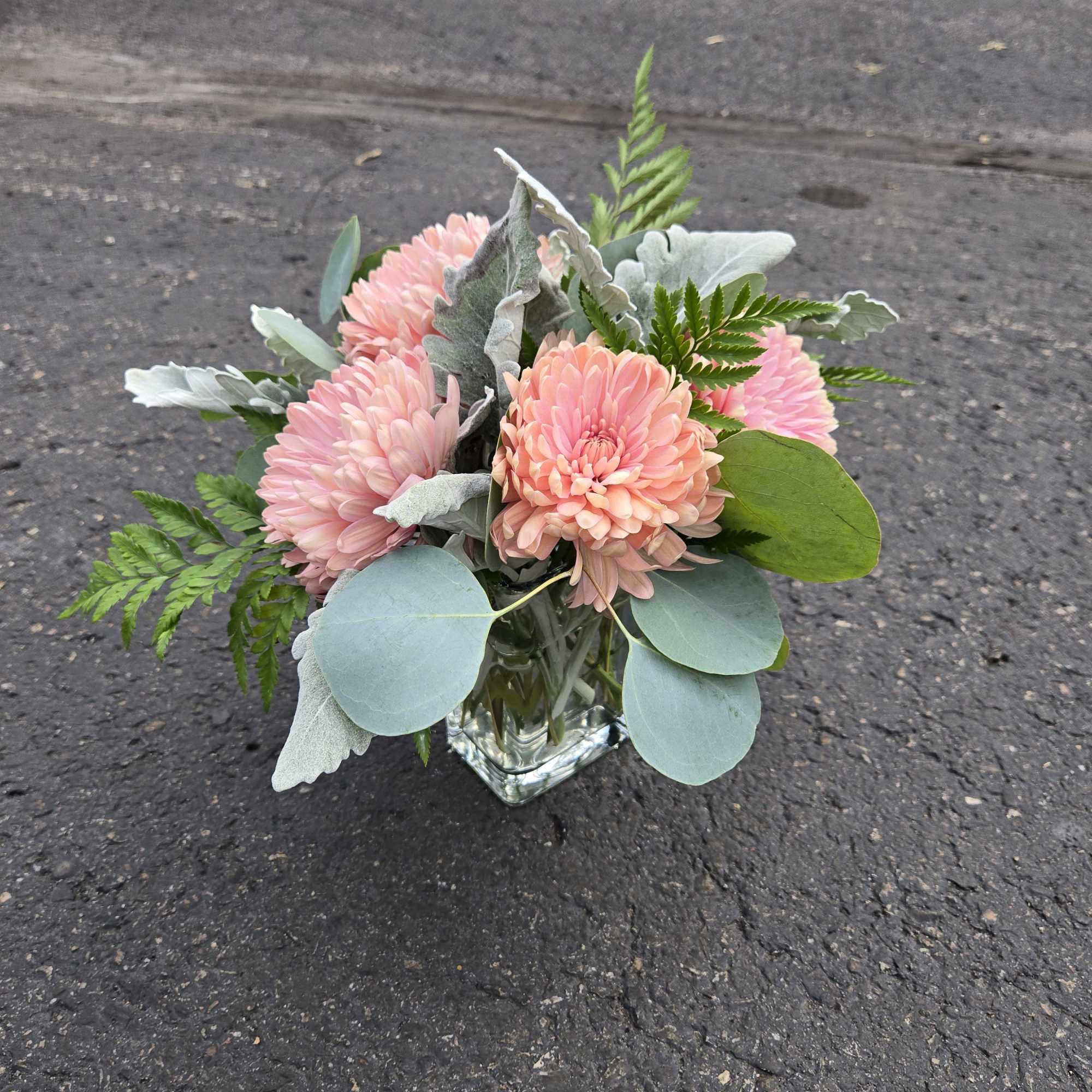Pink chrysanthemum bouquet in a clear square vase with silver foliage