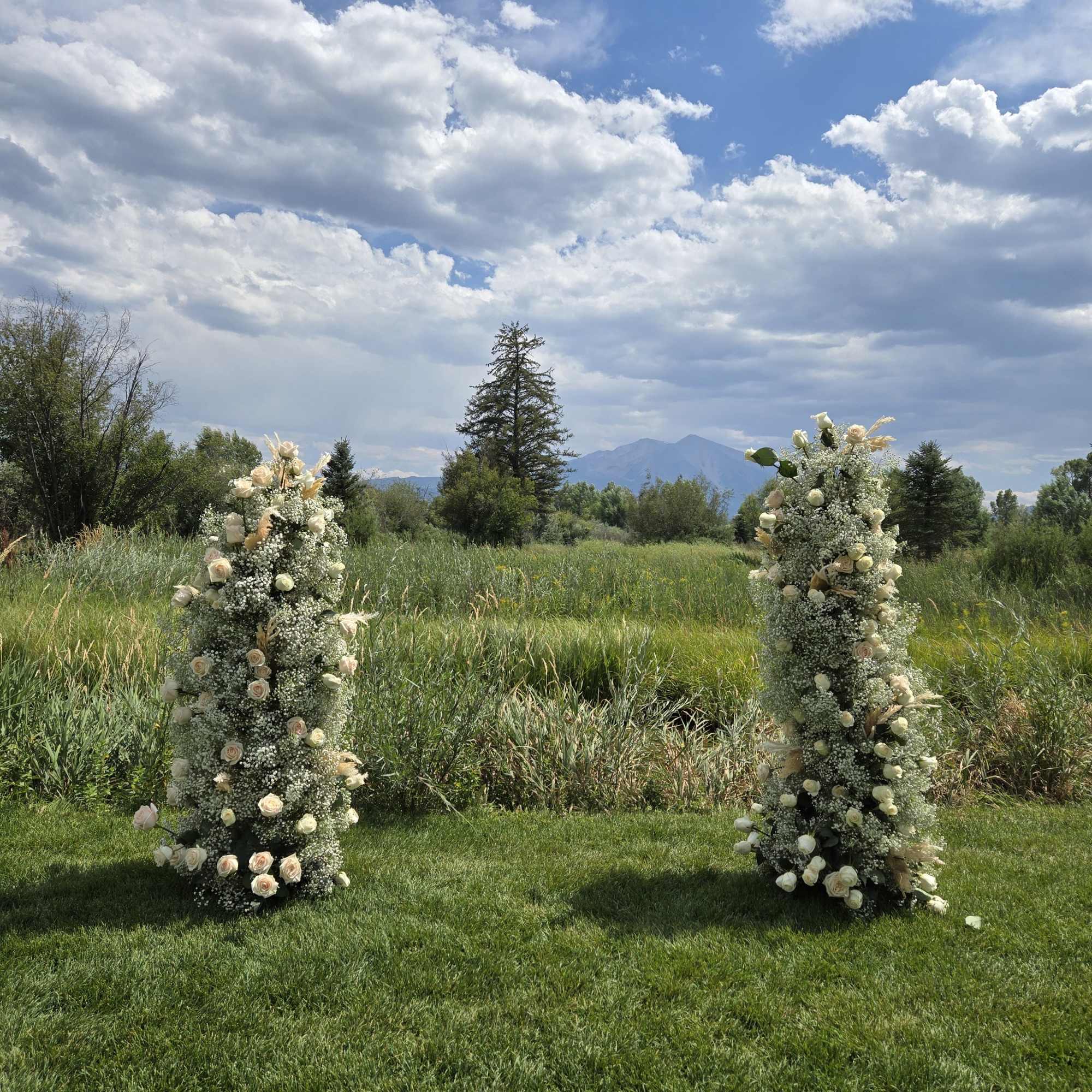Two tall floral pillars with white and blush flowers in a grassy field