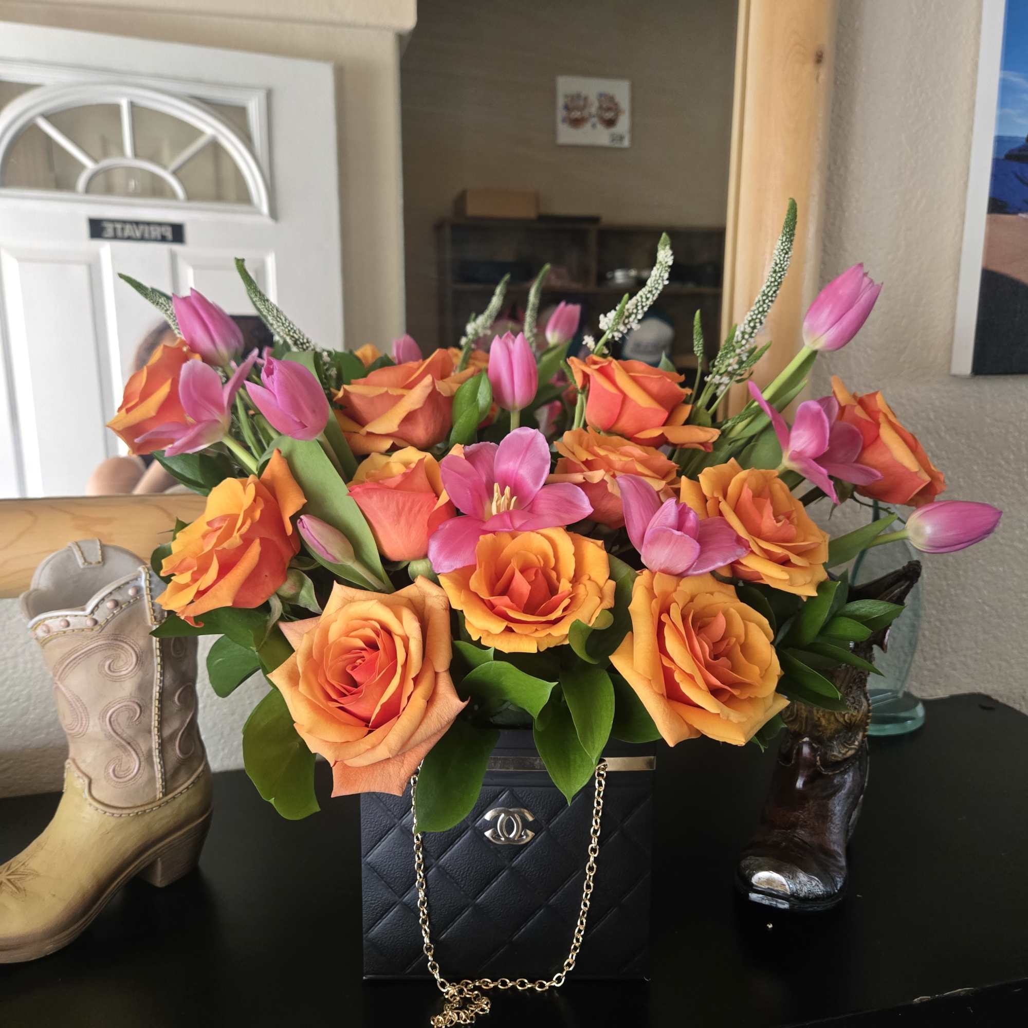 Orange roses and pink tulips arranged in a black box with a gold chain