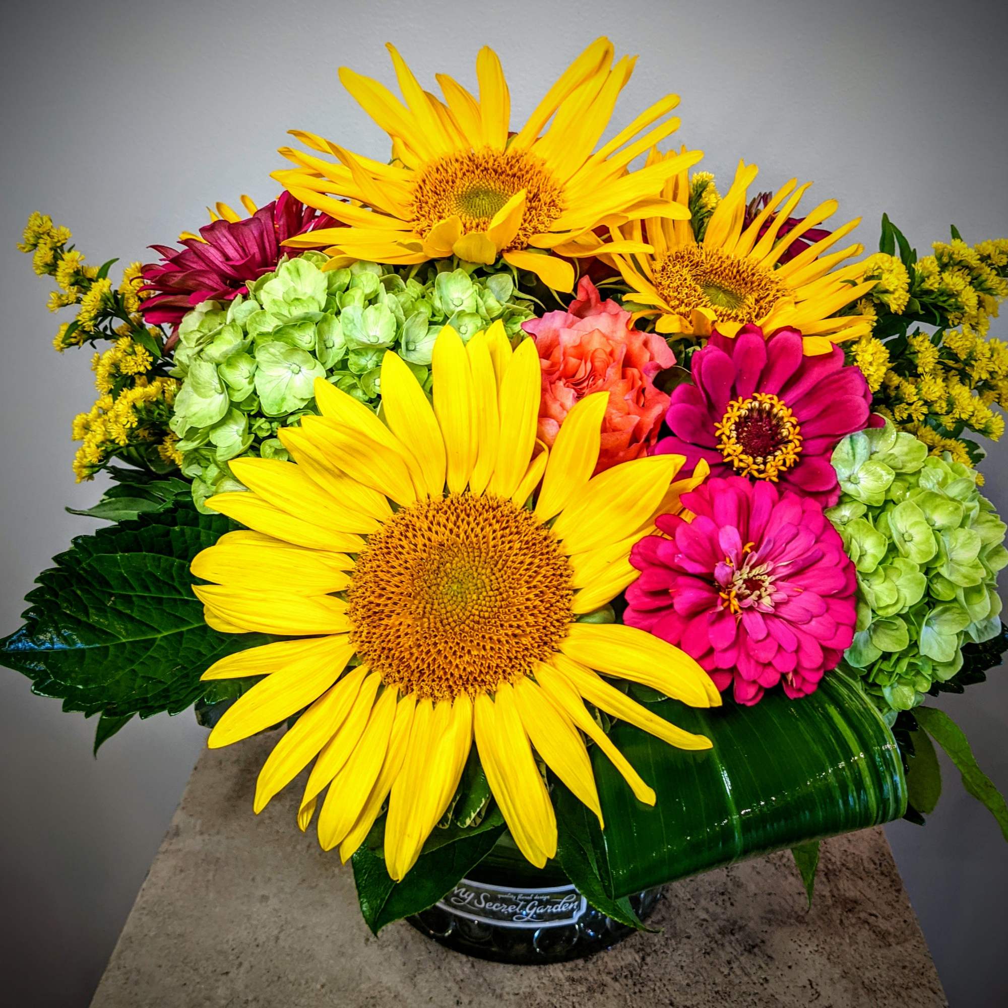 Bright bouquet with sunflowers, zinnias, and hydrangeas in a glass vase